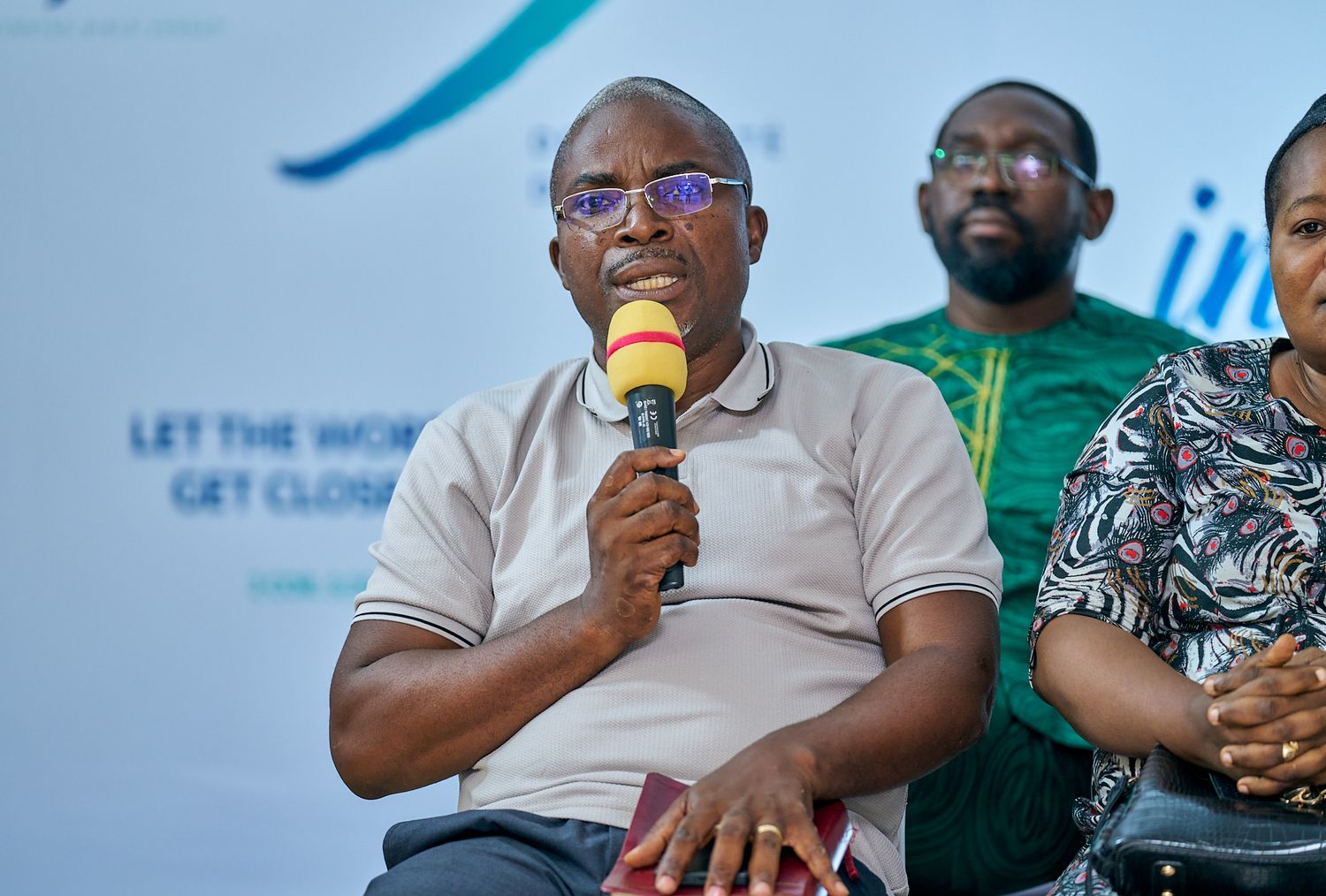 Speaker addressing audience with microphone during sharing moment called intentionnel with teal backdrop and banner.