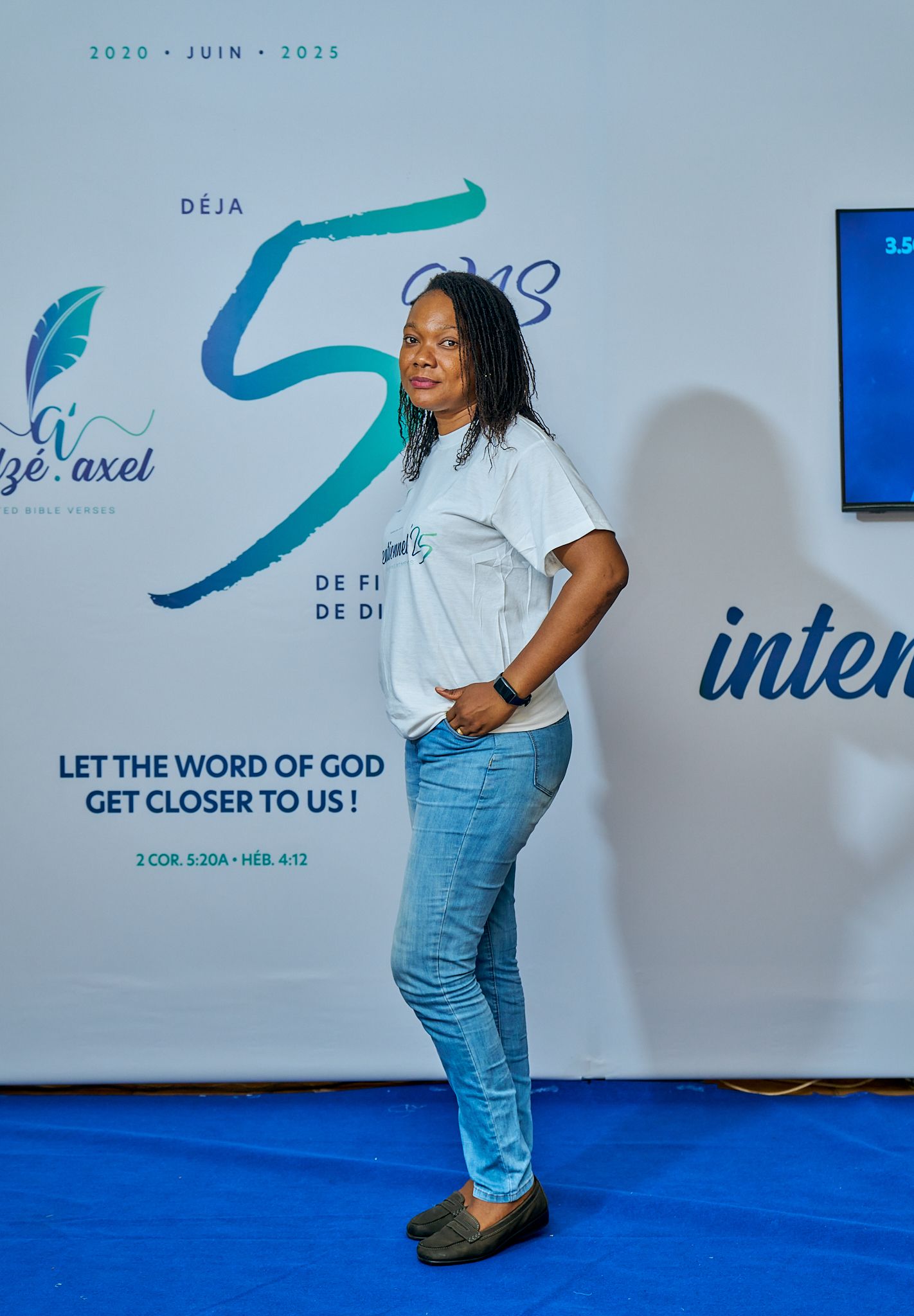 Person in white shirt and jeans posing playfully against blue and white branded wall during sharing moment called intentionnel