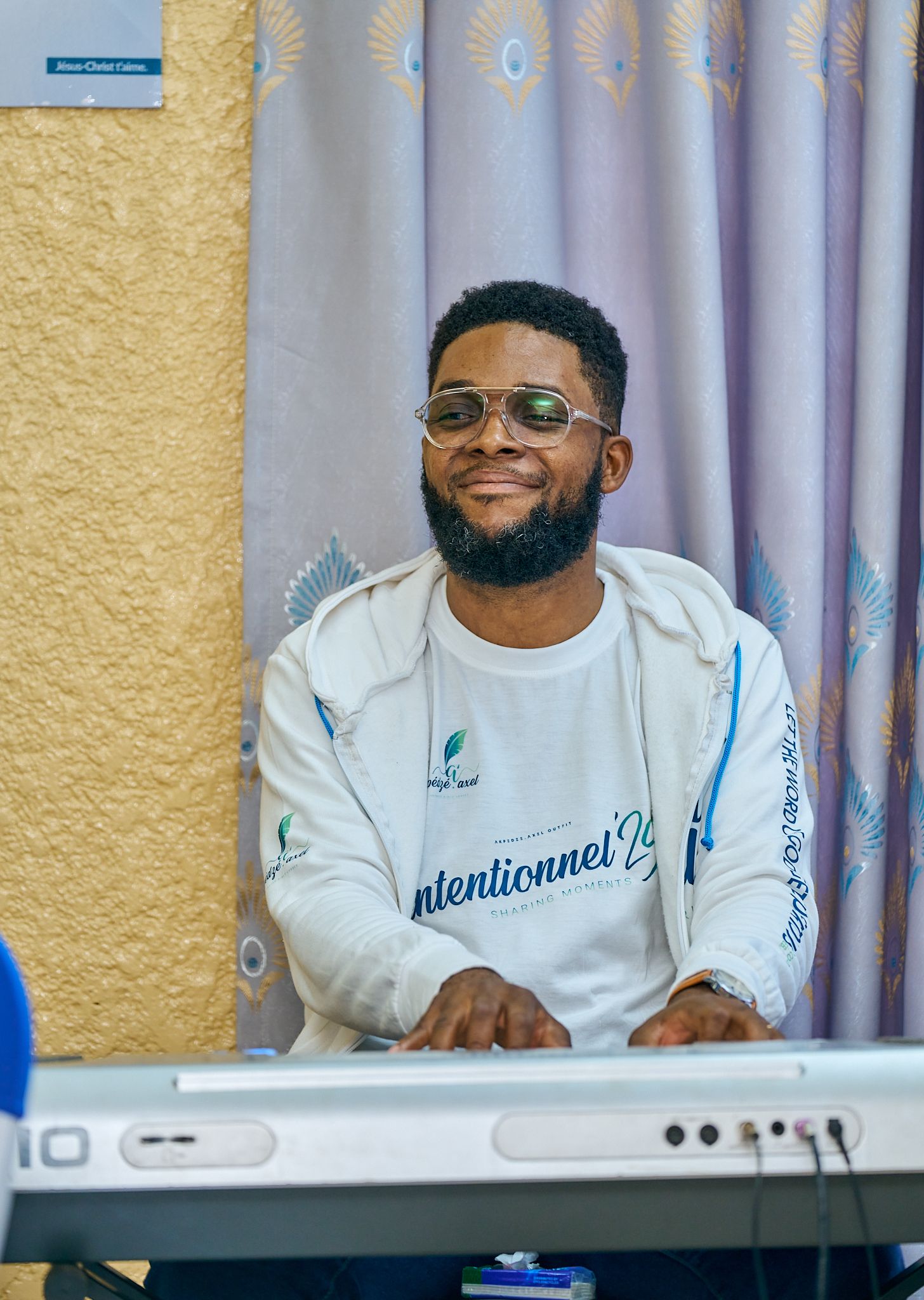 Musician seated at keyboard wearing white sweatshirt with branding at sharing moment called intentionnel