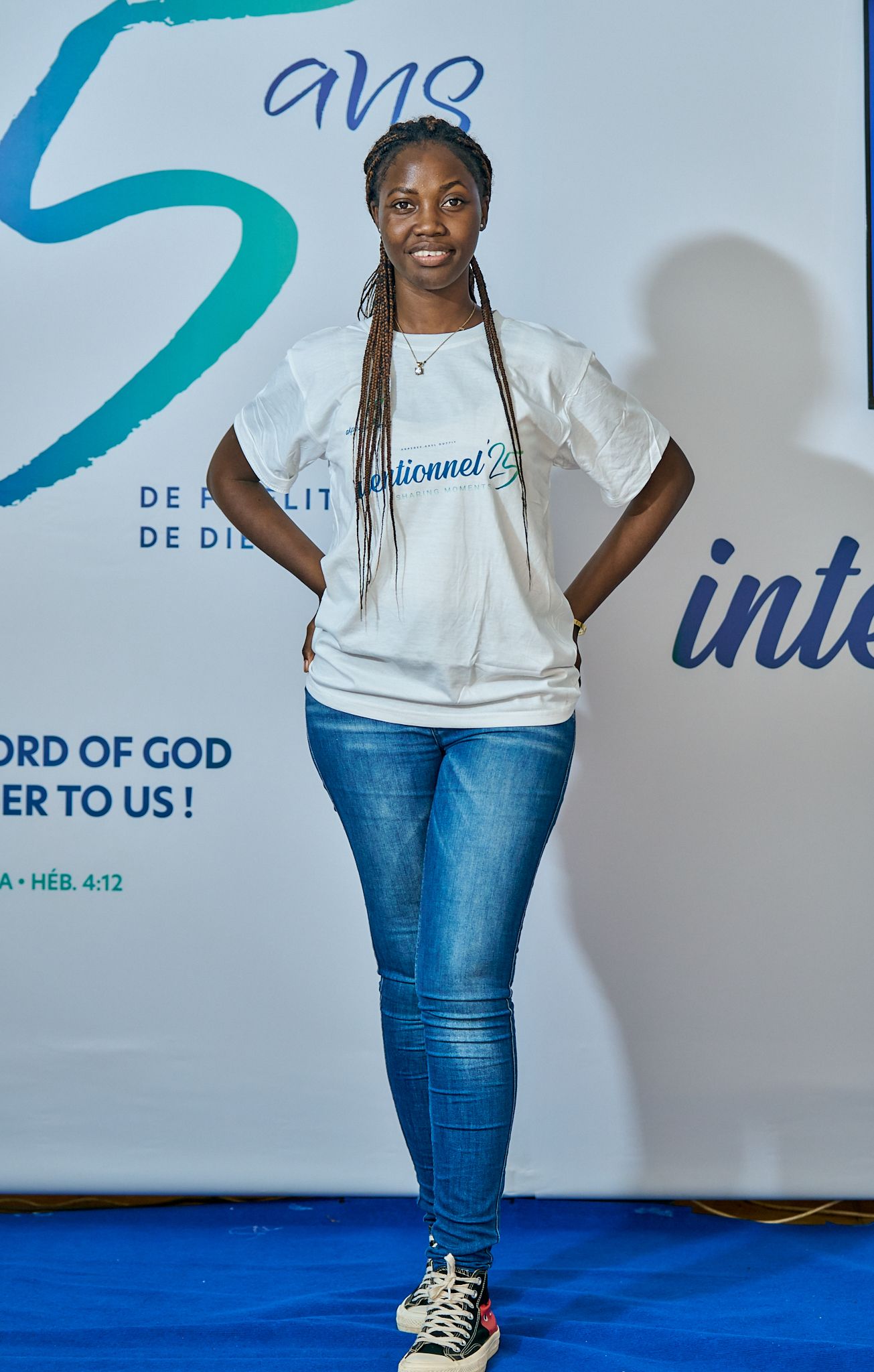 Person striking fun poses in casual white top and jeans against corporate event backdrop during sharing moment called intentionnel