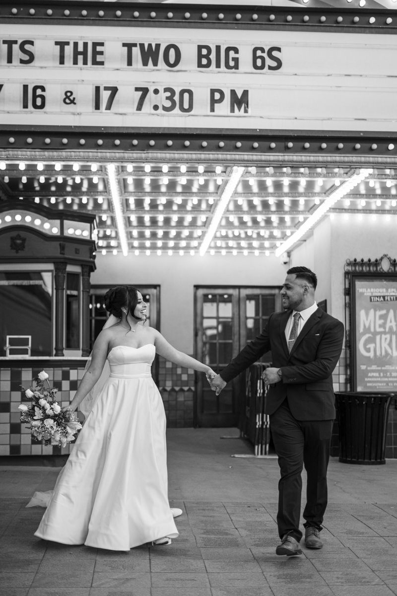 A couple in wedding attire pose beneath a vintage theater marquee sign.