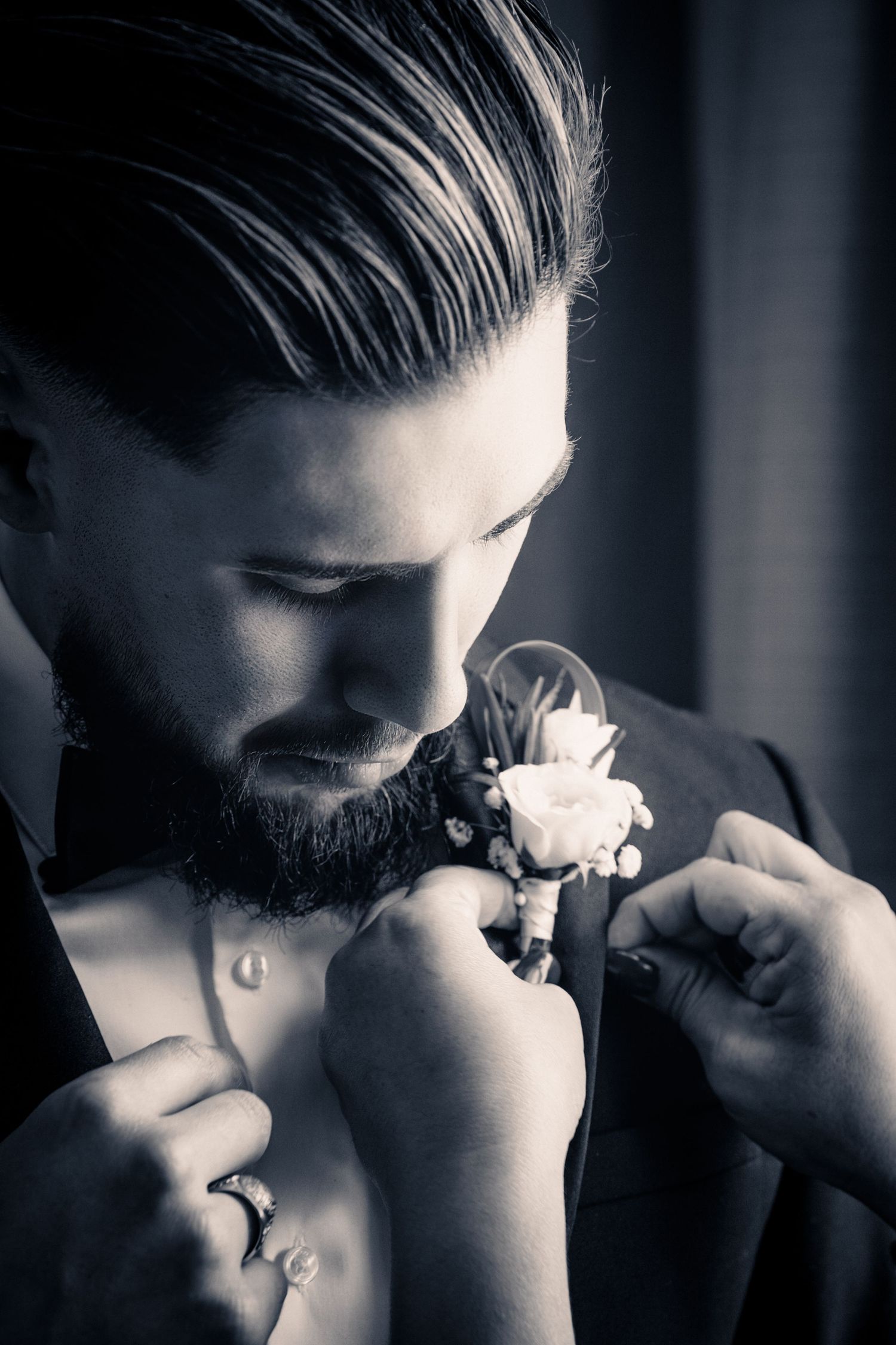 Black and white photo of a bearded groom having a rose boutonniere pinned to his suit lapel.