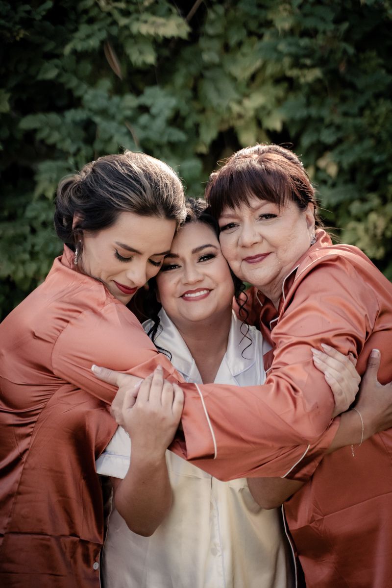 Bridesmaids in coral colored dresses share a joyful group hug.