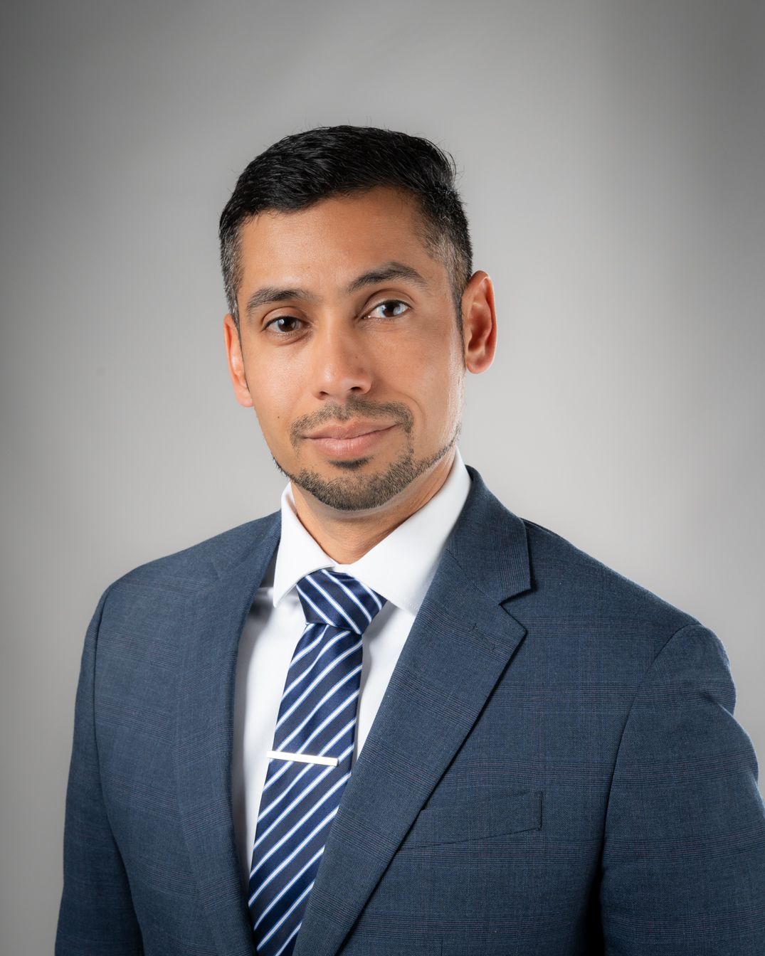Professional headshot series showing a man in a dark suit and striped tie against a gray background from different angles.
