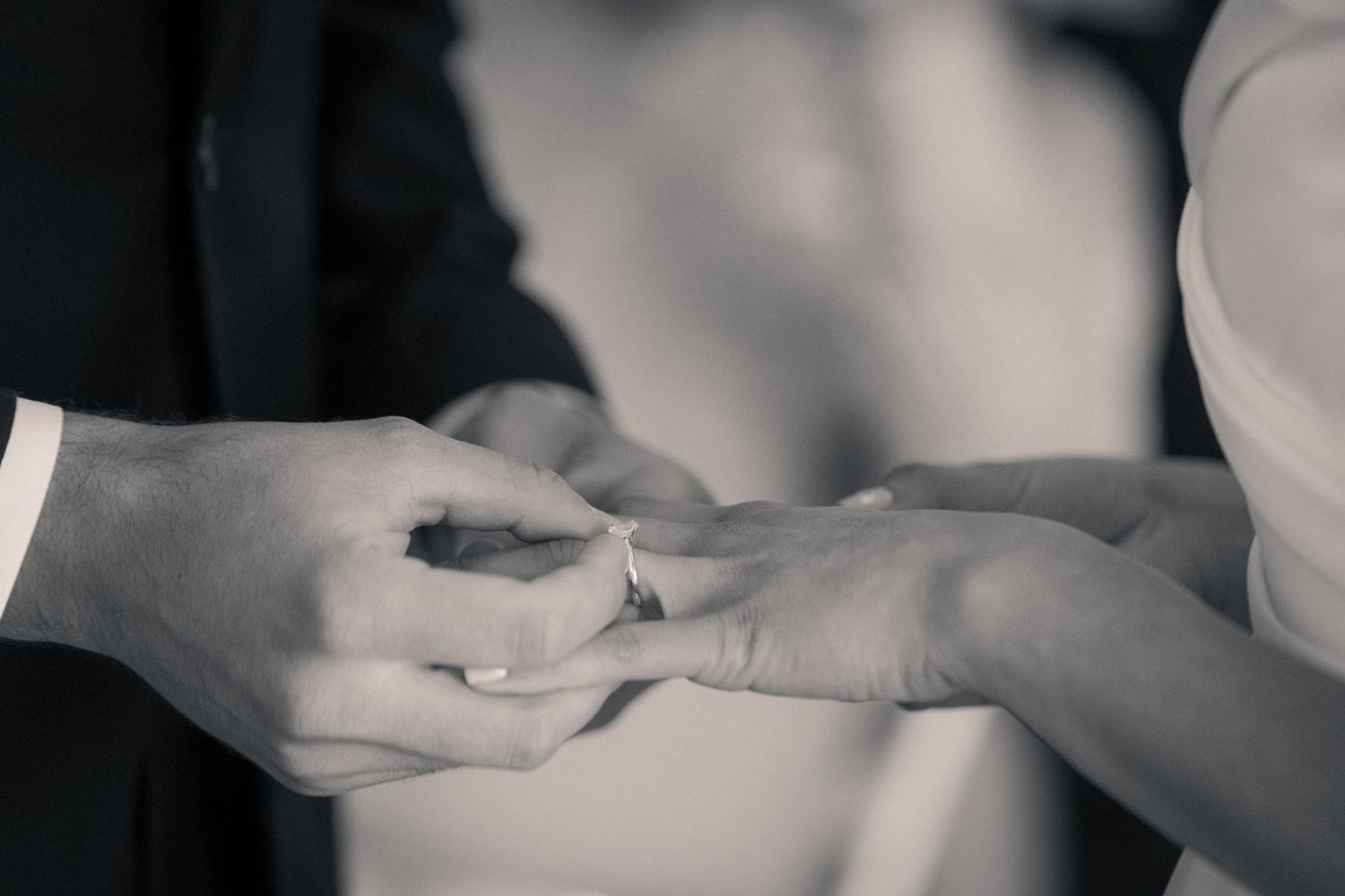 Black and white close-up of hands during a wedding ring exchange ceremony.