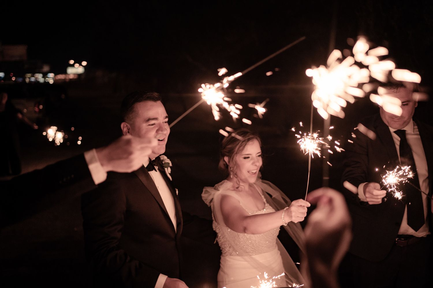 Wedding guests hold sparklers in the dark creating a magical nighttime atmosphere.