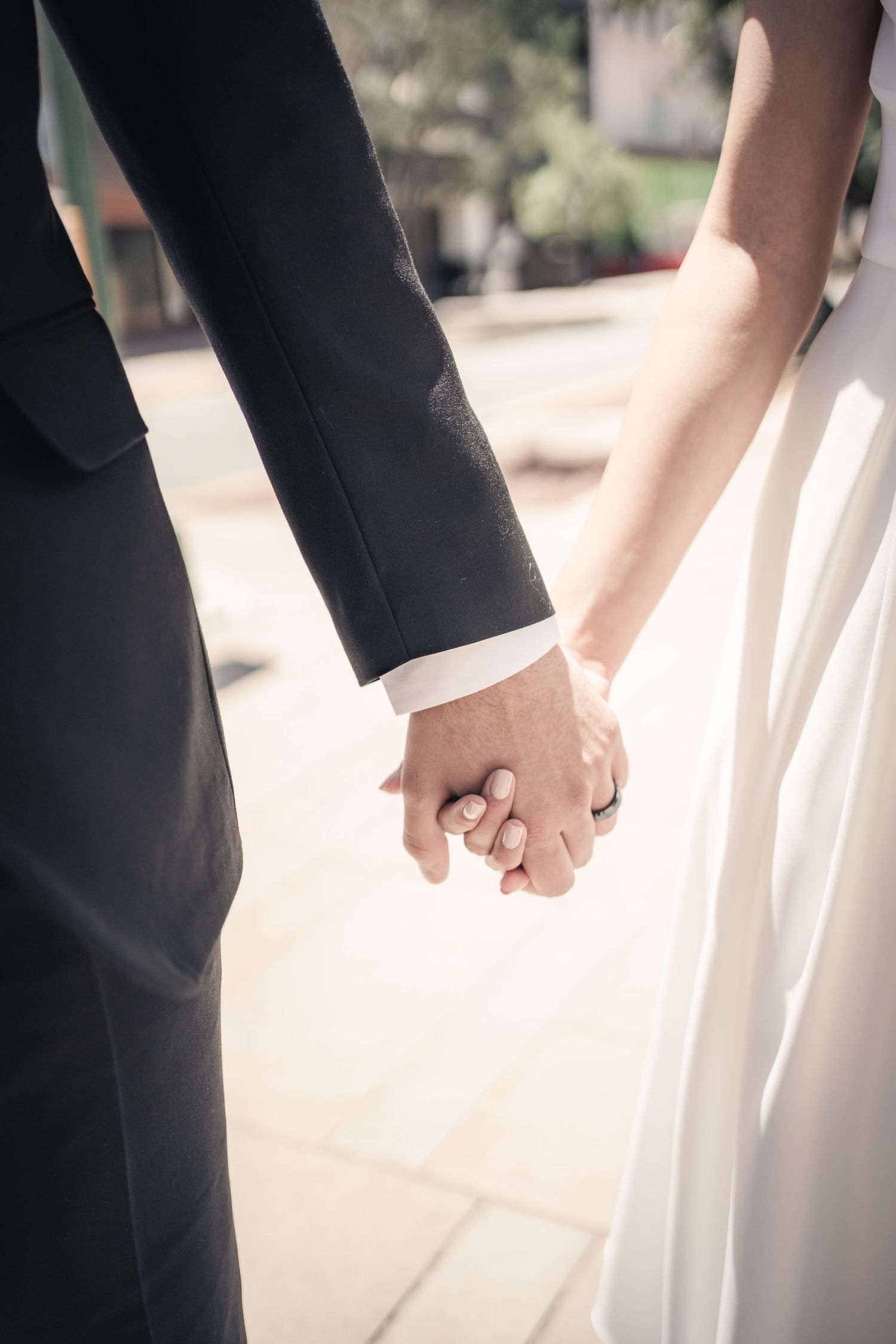 Intimate black and white photo of newlyweds holding hands in formal attire.