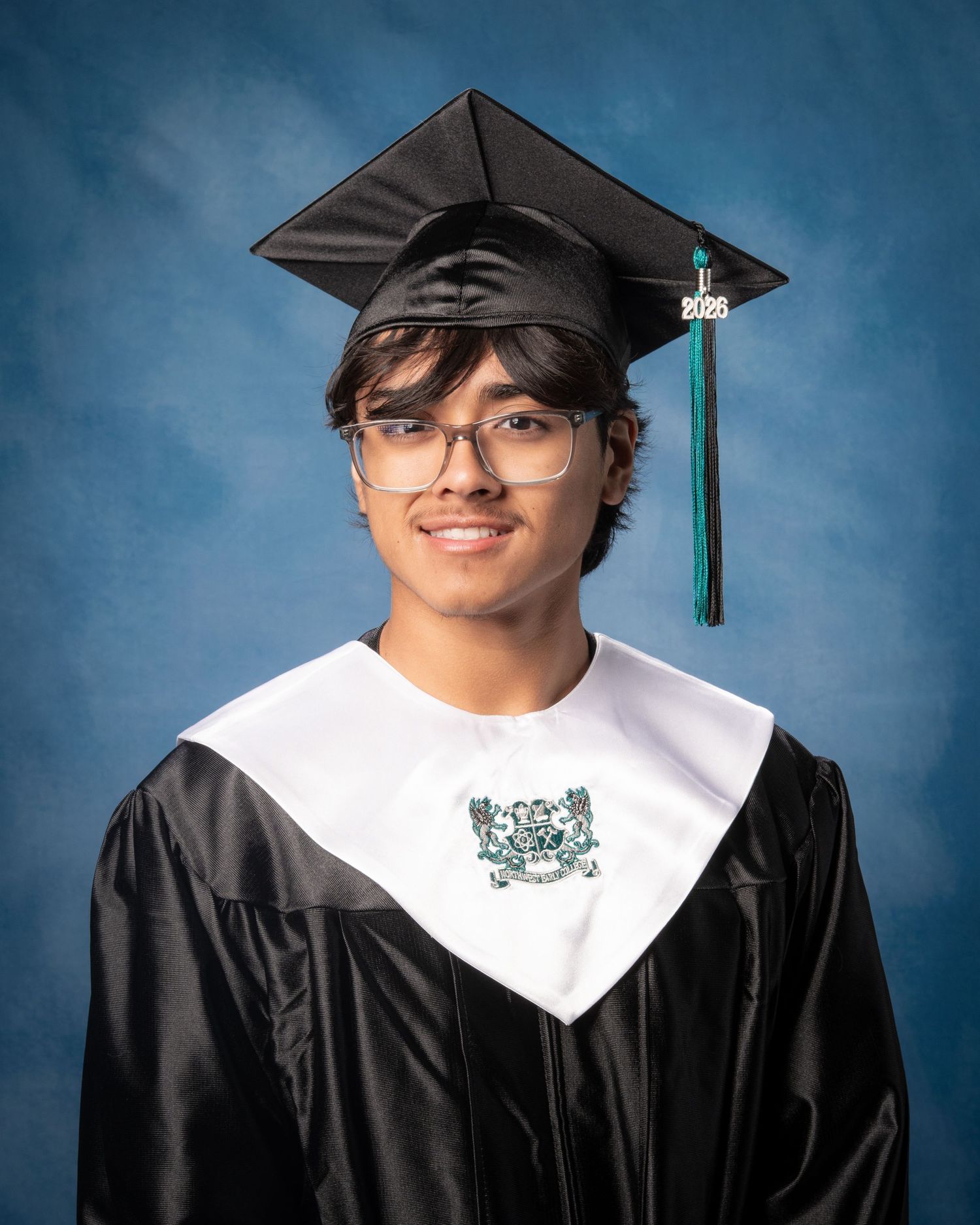 Smiling graduate in black cap and gown with white collar and green tassel for class of 2025 portrait.