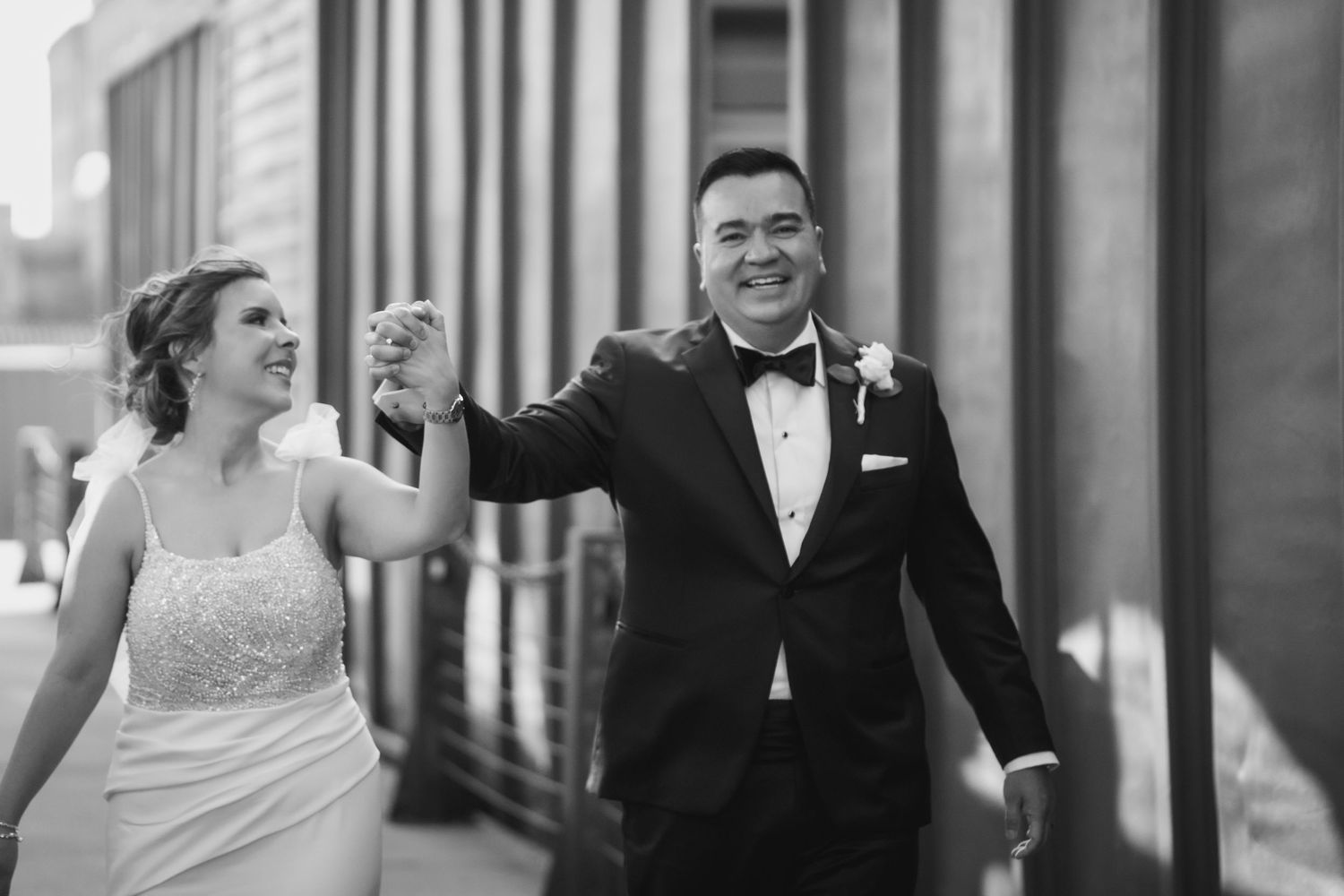 Black and white image of joyful newlyweds walking together outdoors.
