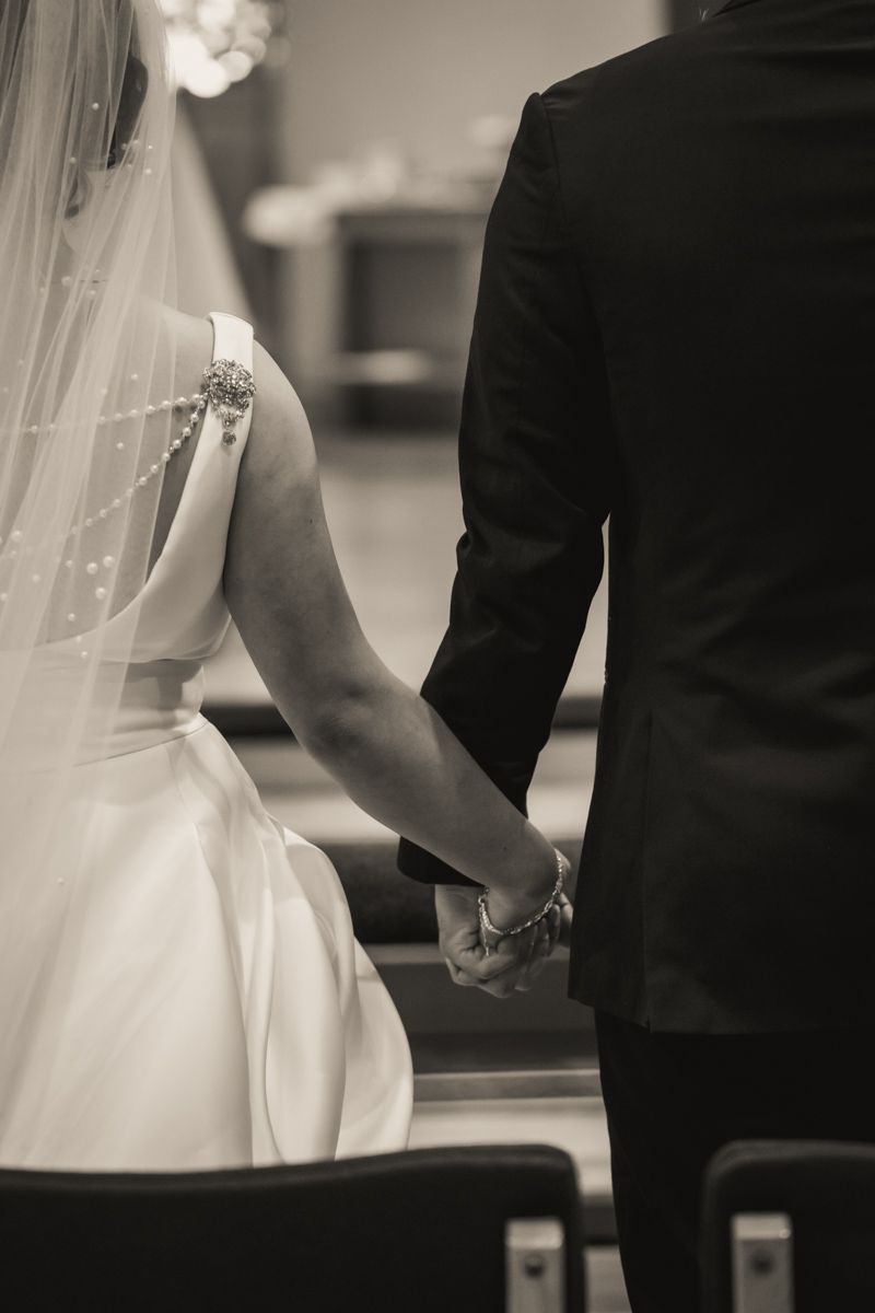 Black and white photo of a bride and groom holding hands during wedding ceremony.