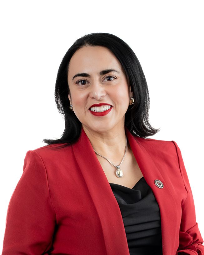 Professional wearing a red blazer and black top poses with a bright smile against white background.