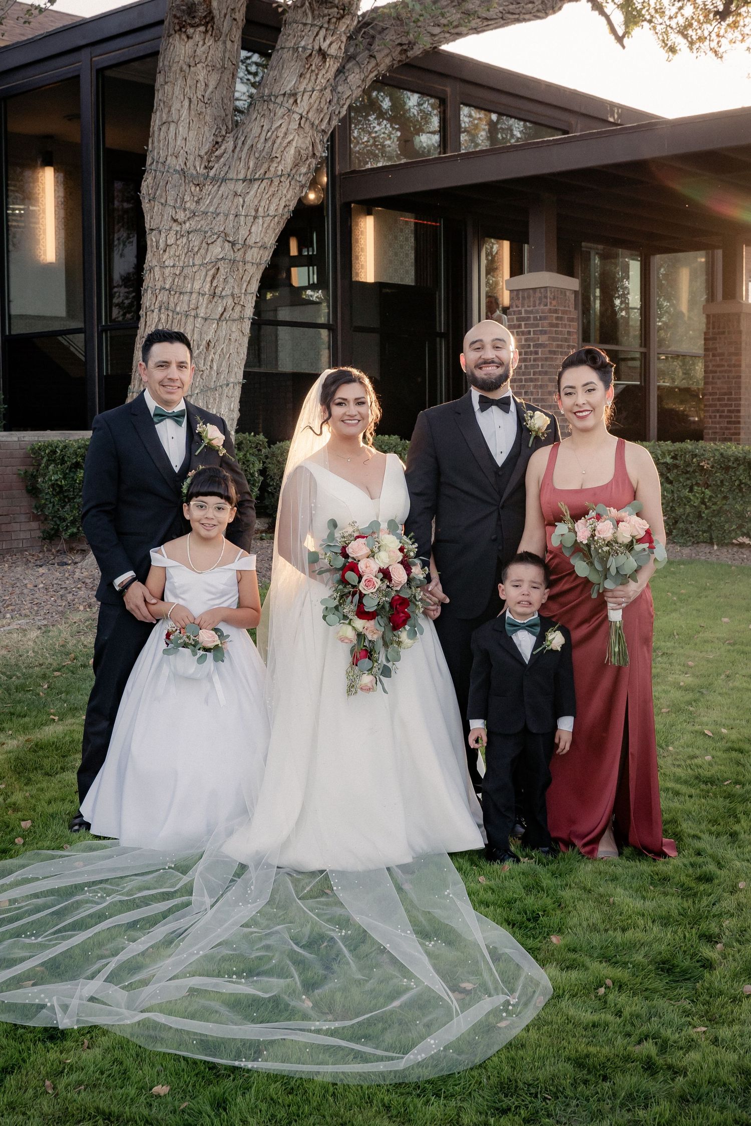 Wedding party poses together outdoors with cathedral veil and floral bouquets.