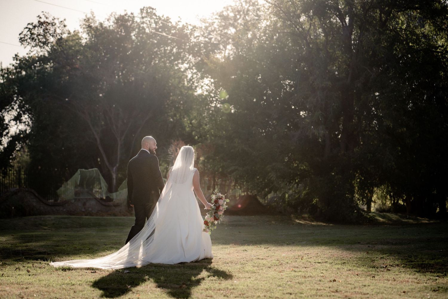 Silhouetted couple walking on grass during golden hour wedding photography.