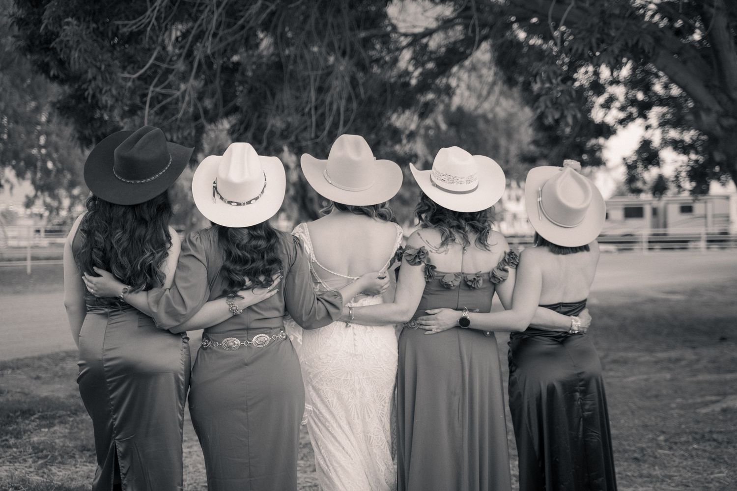 Black and white photo of five people wearing cowboy hats standing together with arms around each other.