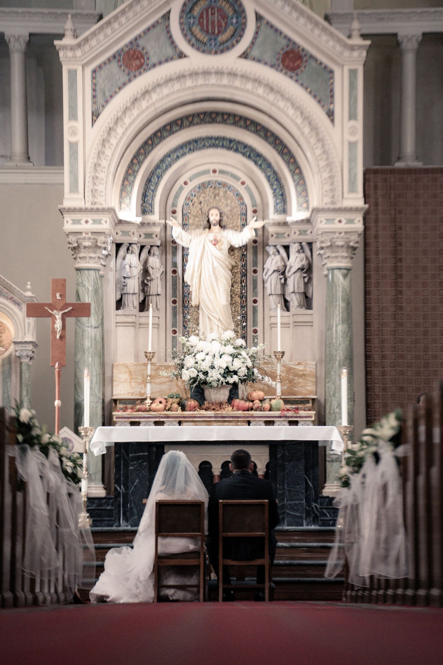 Ornate Catholic church interior with grand altar, statues and marble columns during a wedding ceremony.