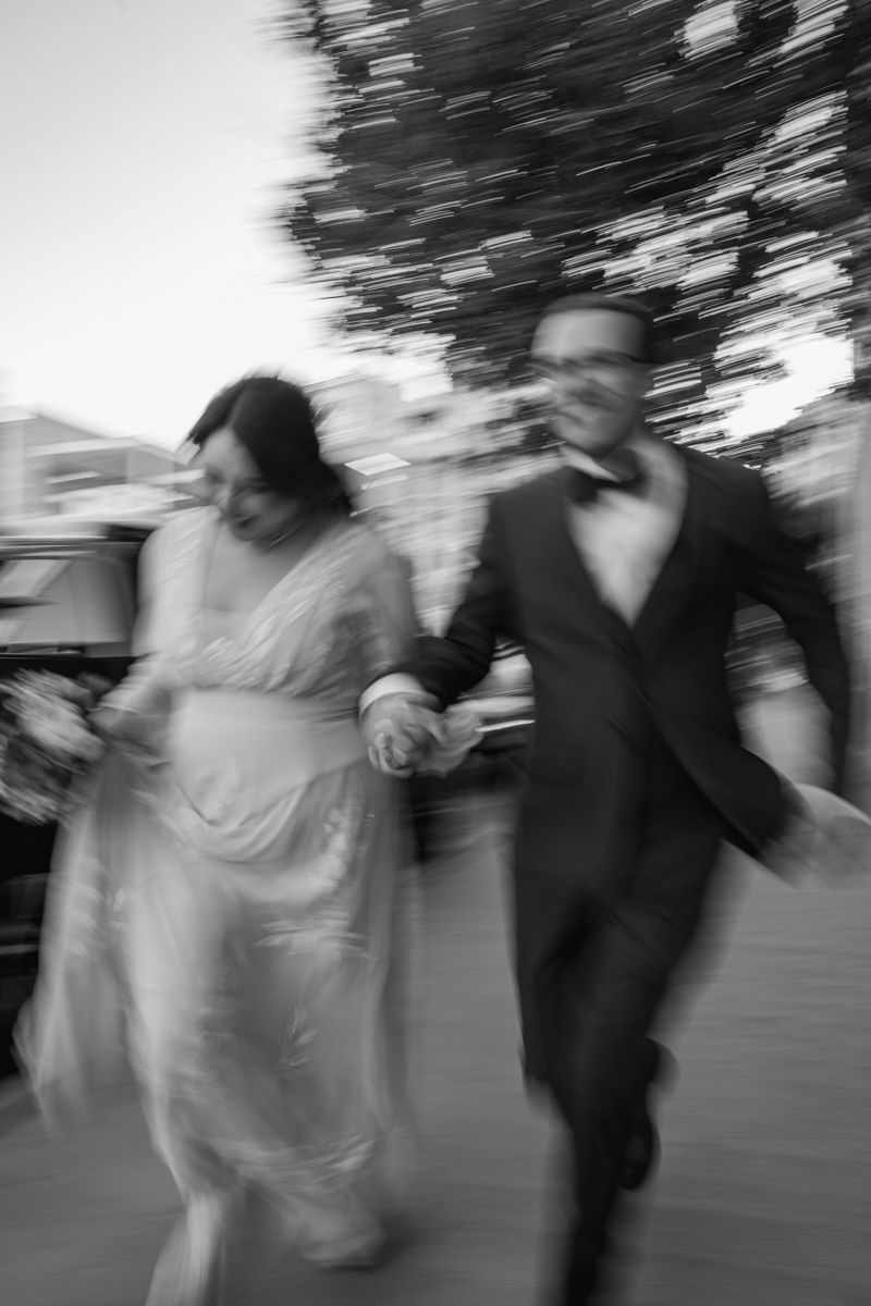 Motion-blurred black and white photograph of a couple running together outdoors.