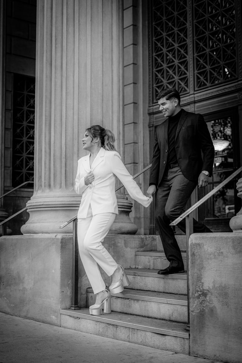 Black and white photo showing couple ascending stone stairs with classical columns.