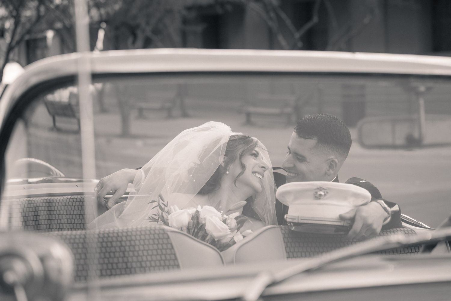 Black and white photo of a bride and groom sharing a romantic moment in a vintage convertible car.