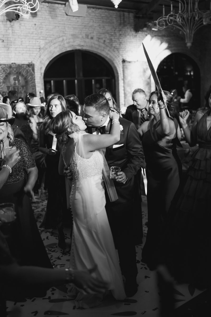 Wedding reception dance floor filled with guests celebrating under brick archways in black and white.