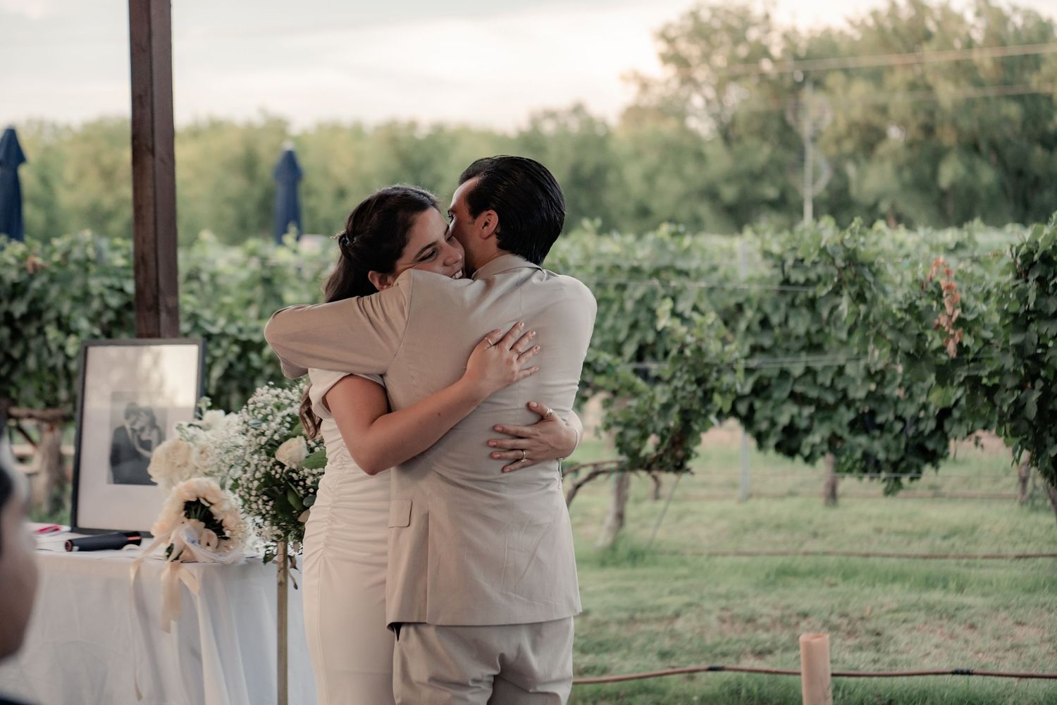 Wedding couple embracing outdoors in a vineyard setting during golden hour.