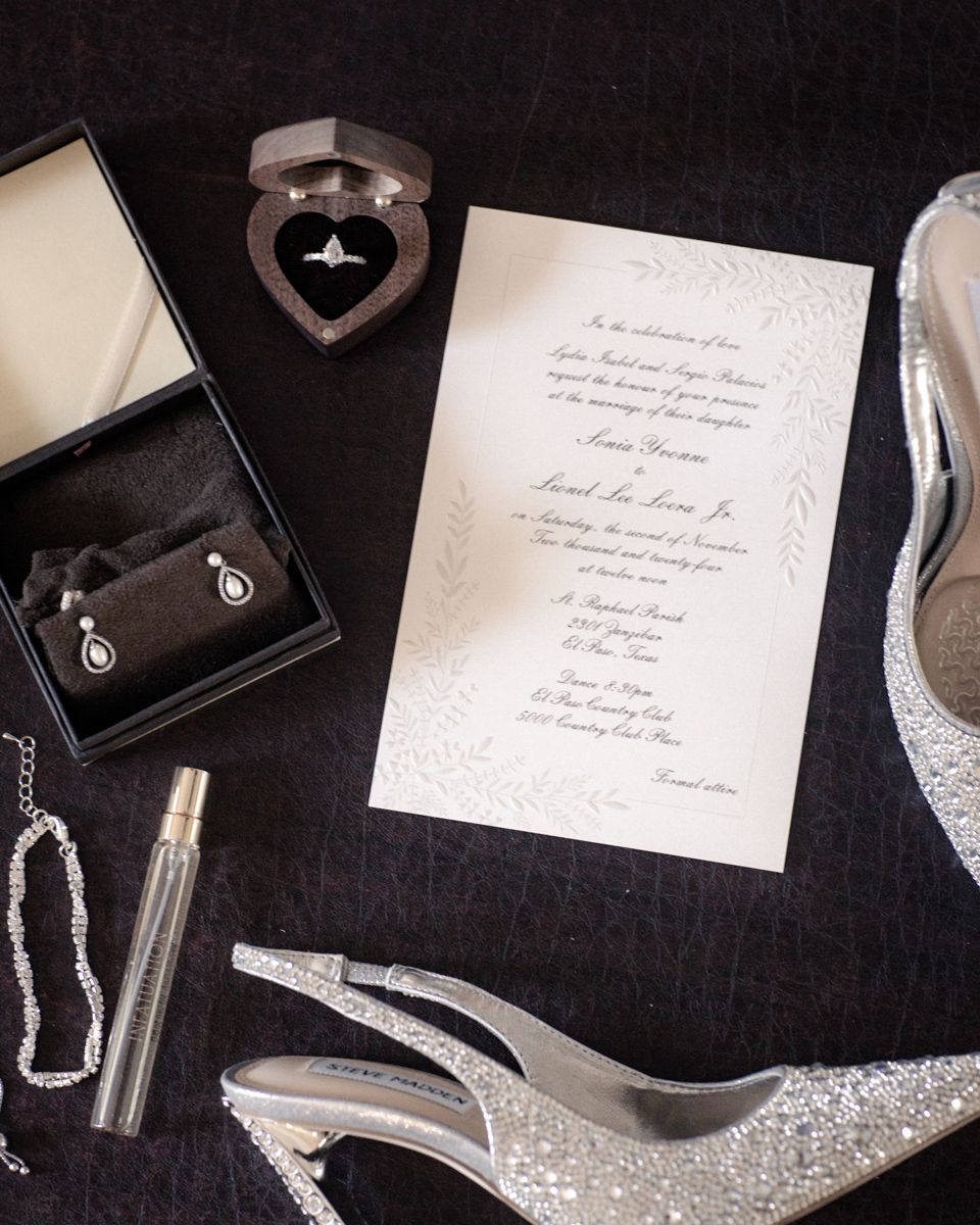 Wedding details including jewelry, invitations, shoes and accessories arranged on black background.