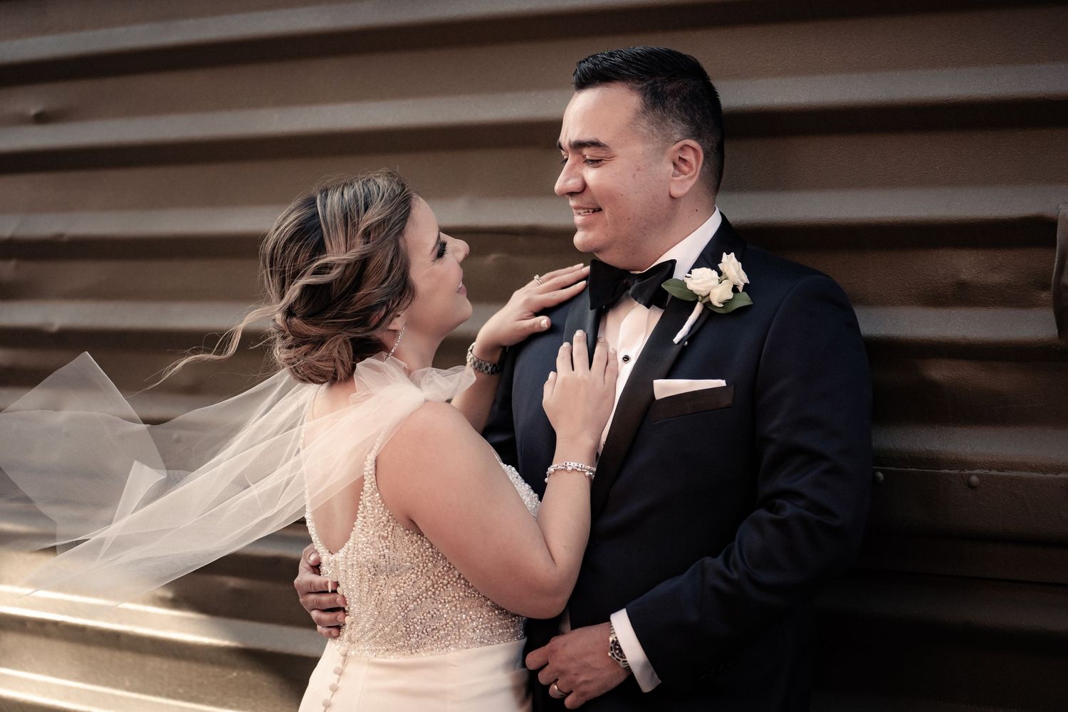 Romantic moment between newlyweds with bride's veil flowing in soft lighting.
