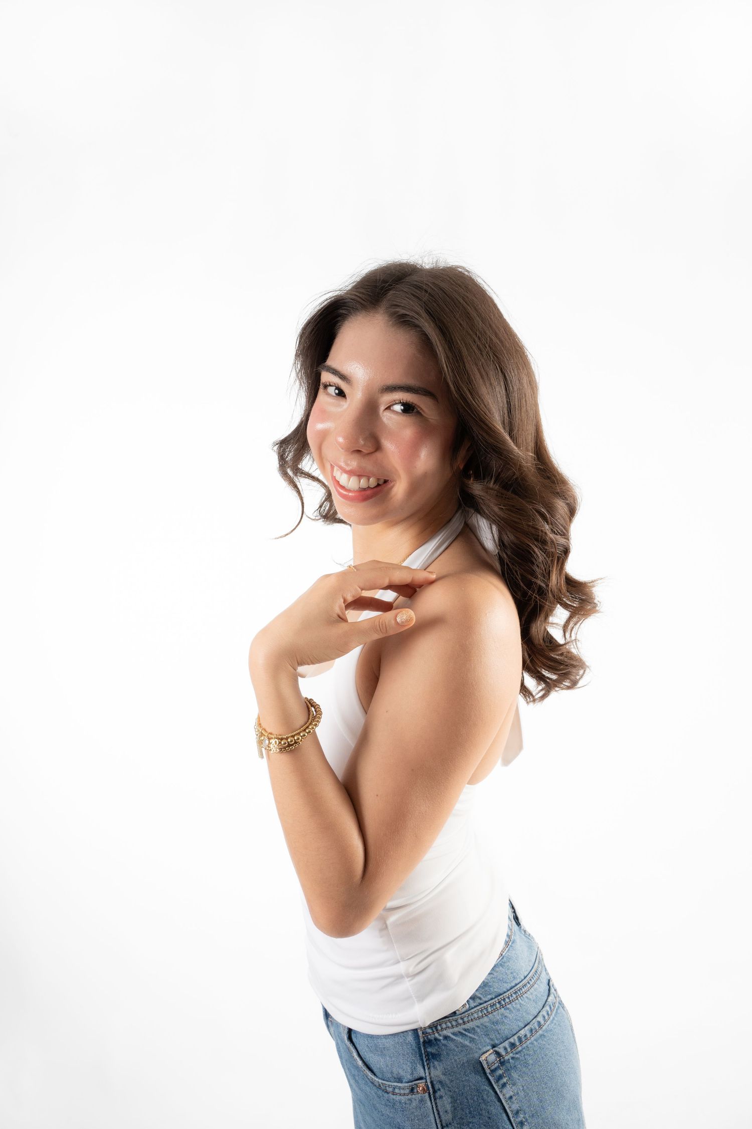 Smiling young Asian woman in white tank top and jeans posing confidently against a white background.