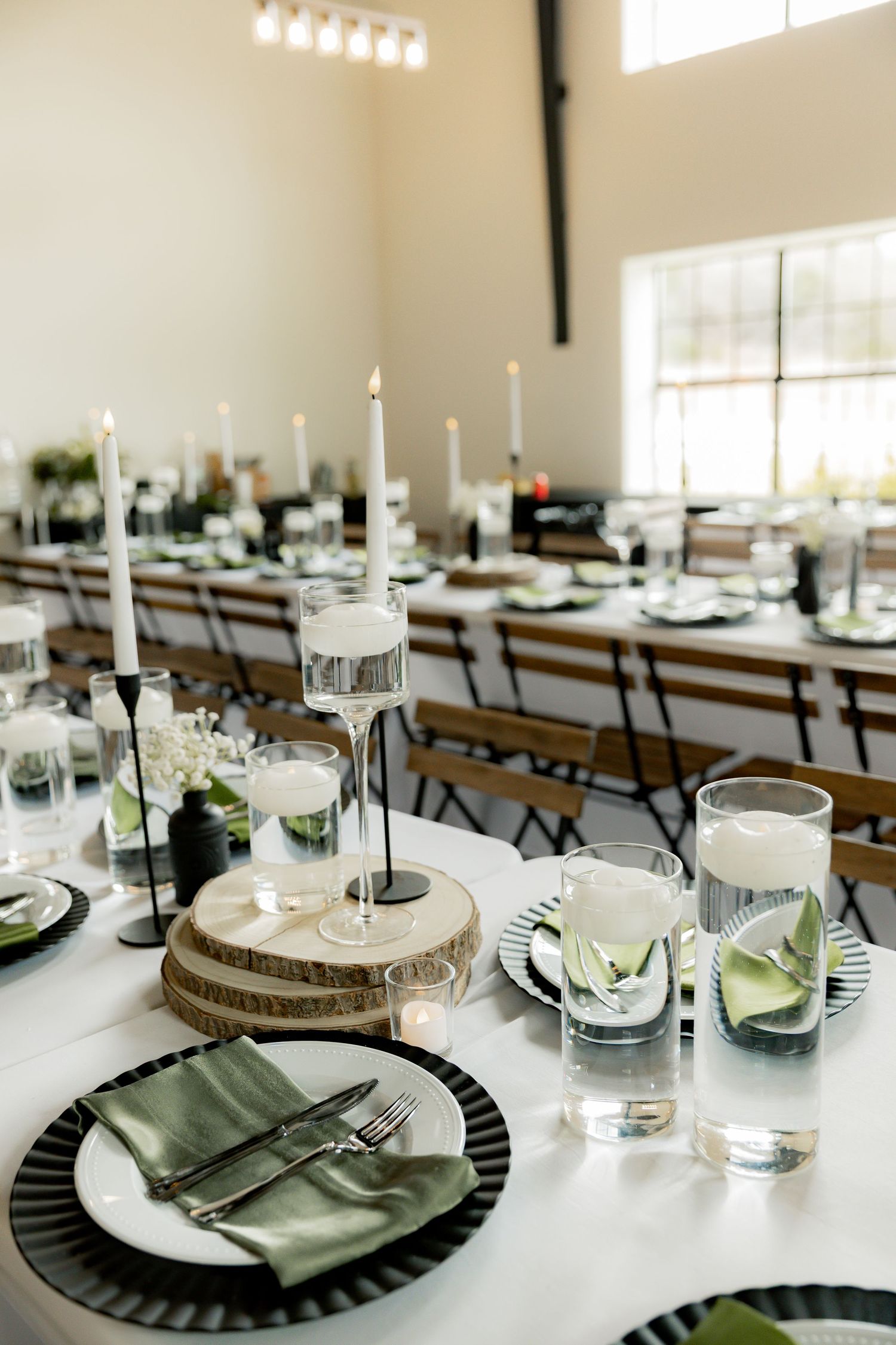 Elegant wedding reception table setting with black charger plates, green napkins, white candles, and floral centerpieces.