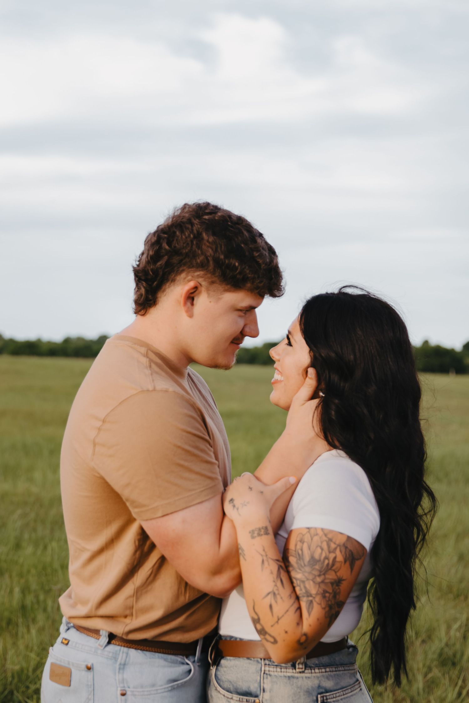 A couple sharing an intimate moment in a grassy field wearing matching casual outfits.