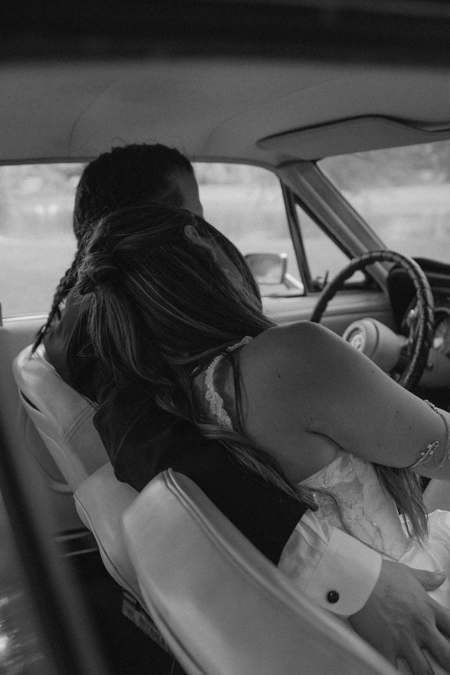 Black and white photo of bride in white dress reclining across car seats.