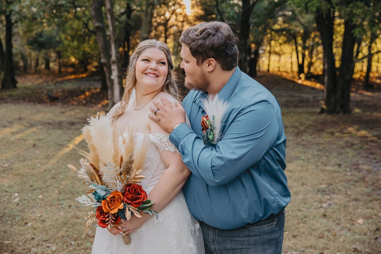 Bride and groom share a tender moment outdoors during golden hour, bride holding a fall bouquet with roses and pampas grass.