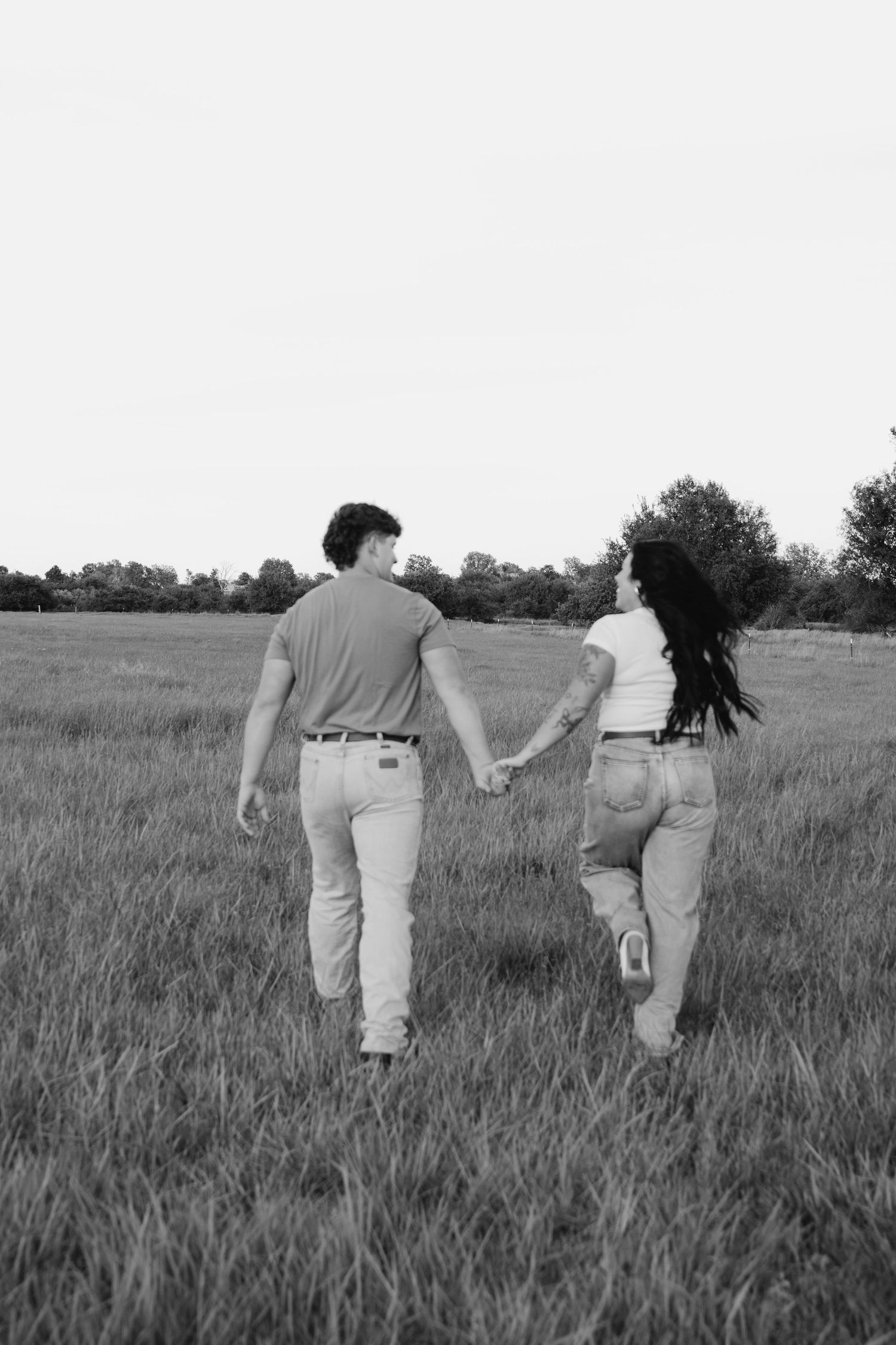 A romantic couple walking hand in hand through a grassy meadow at sunset.