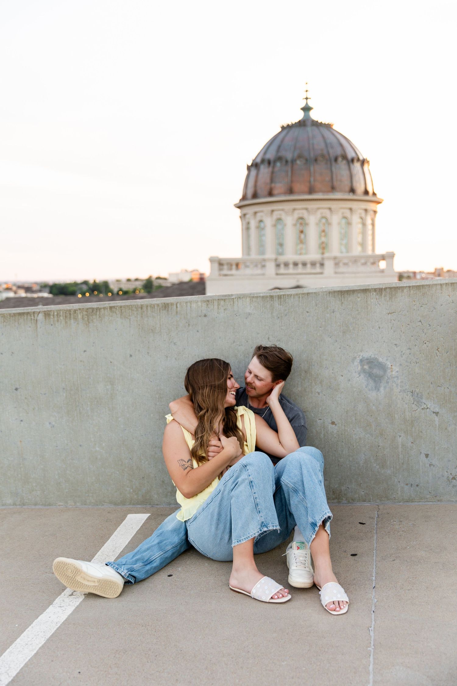 Couple sitting together on rooftop parking deck with historic domed building in background at golden hour.