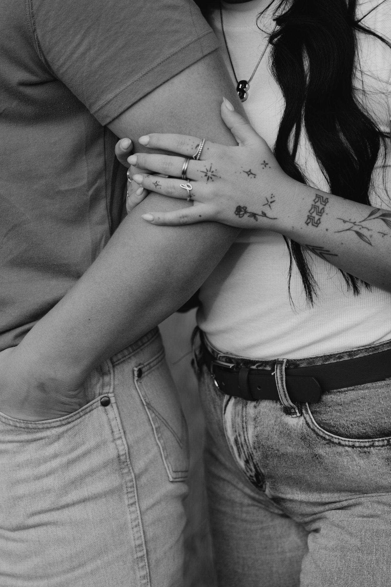 A black and white close-up of hands with tattoos and rings showing affection.