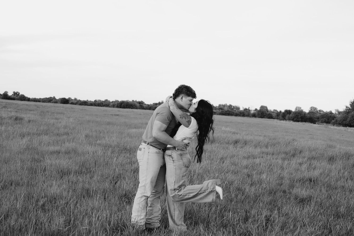 A couple sharing an intimate moment while embracing in an open field.