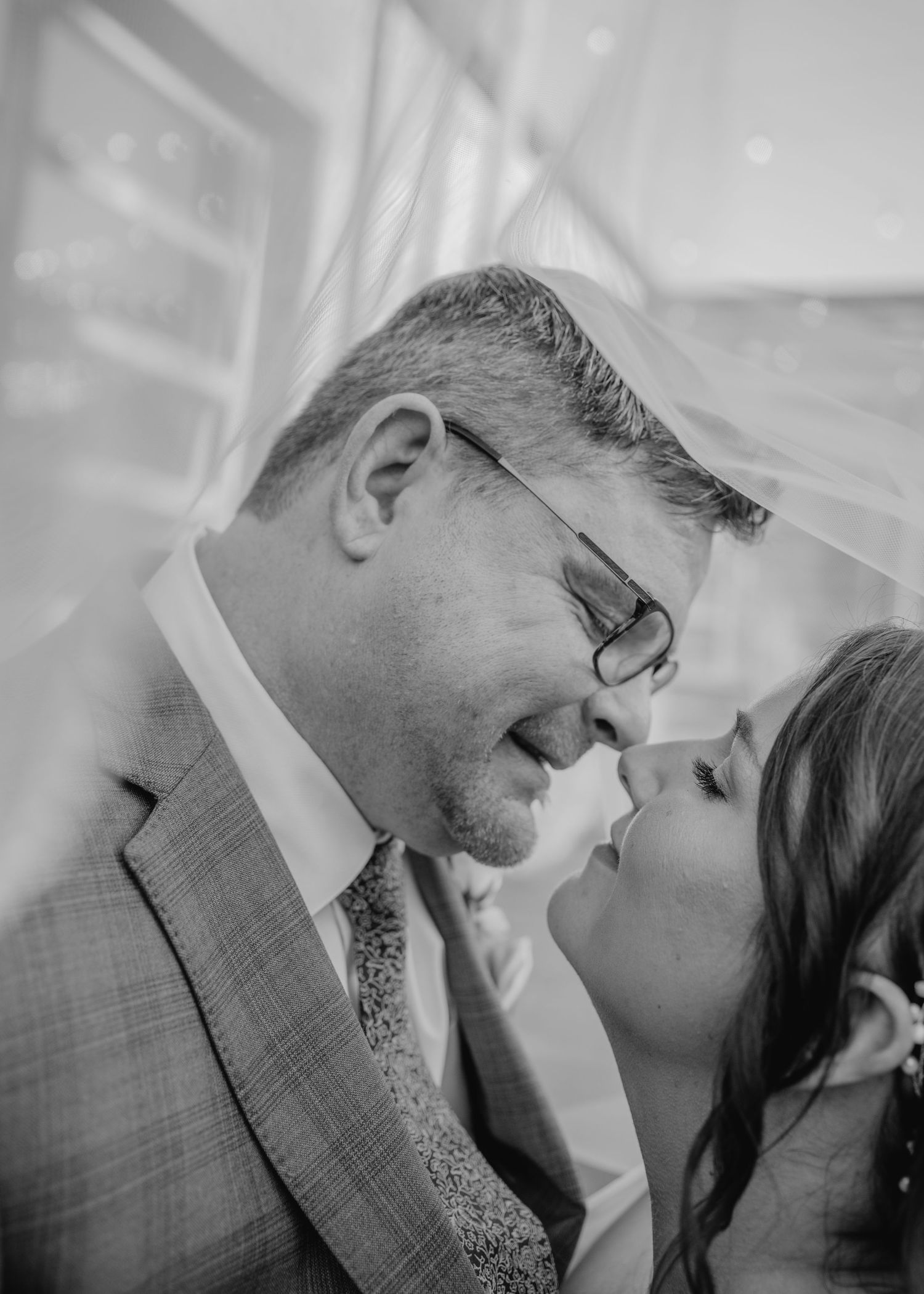 Black and white wedding photo of bride and groom sharing an intimate moment under a veil.