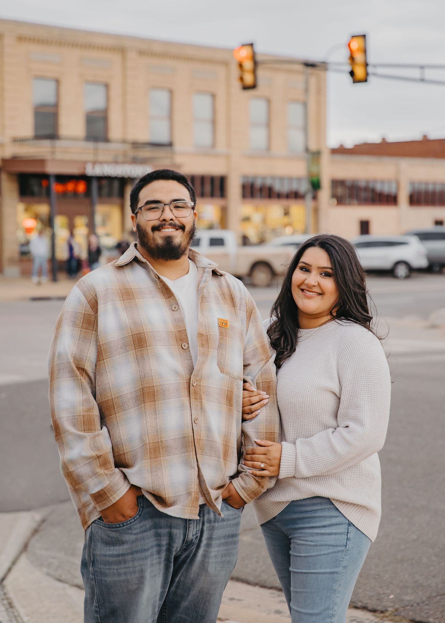 A couple in coordinating plaid and gray outfits walk together on a city street at sunset.