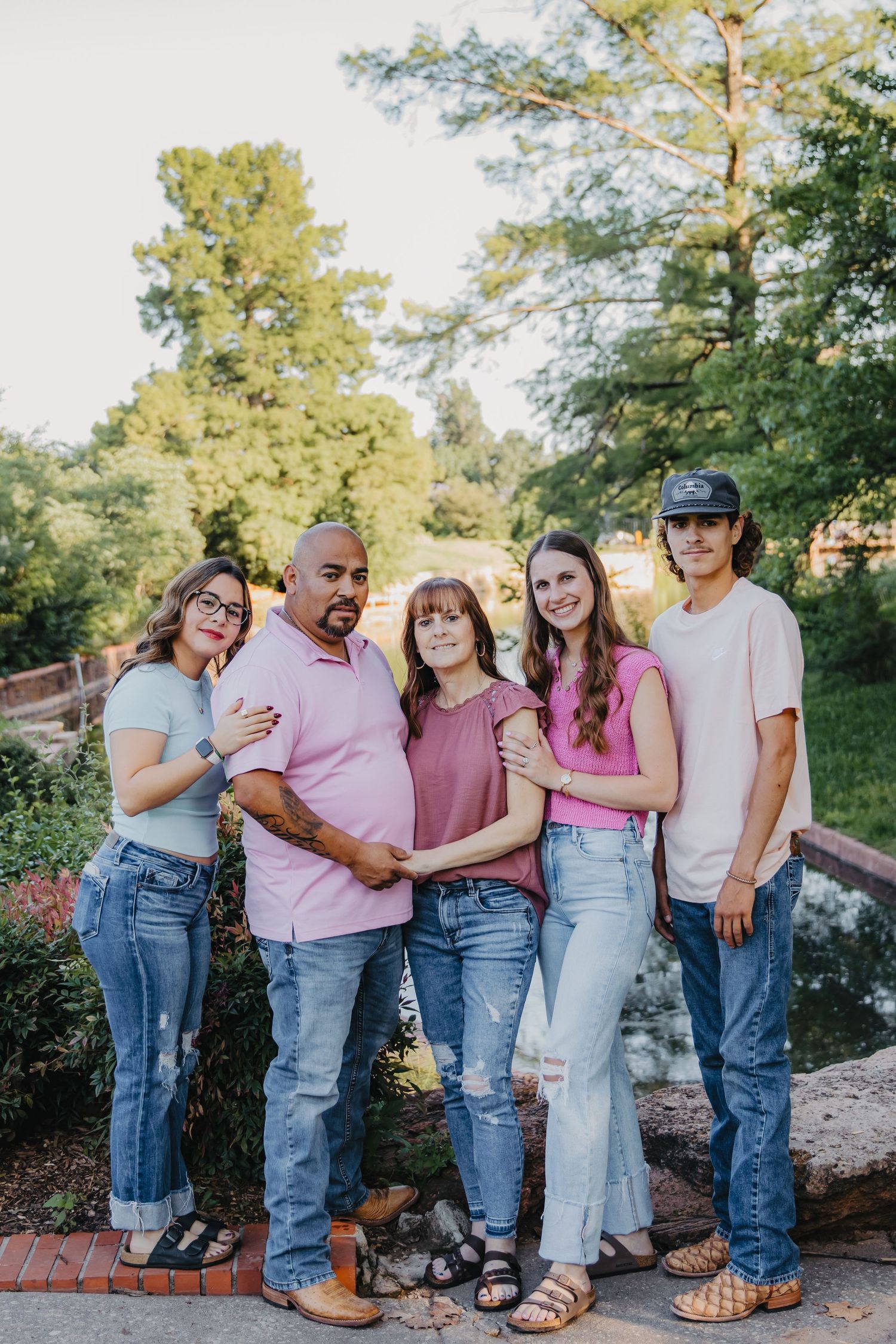 Group of five people standing together outdoors on a sunny day with trees in background.