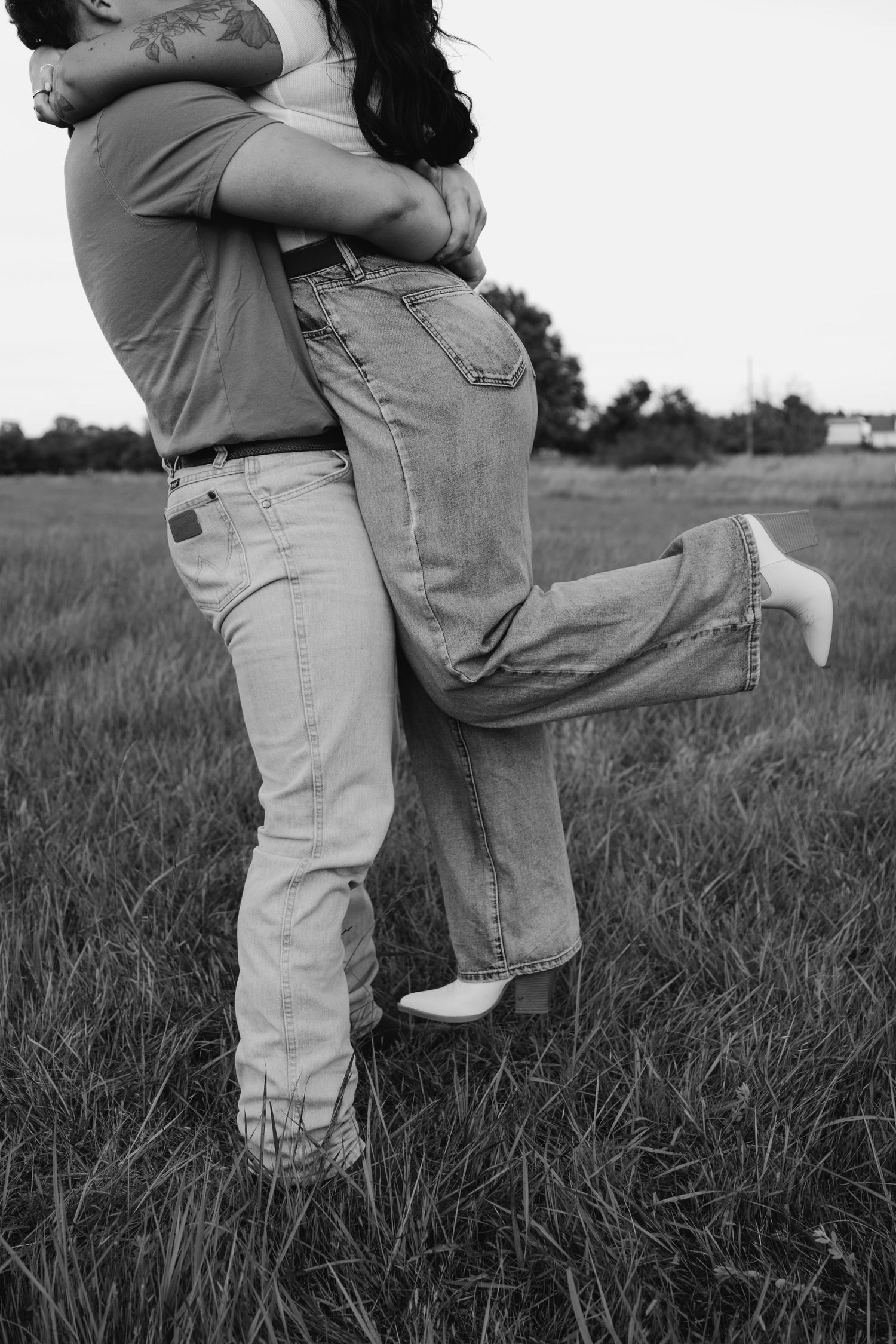 A black and white photo of a couple embracing in a grassy field.
