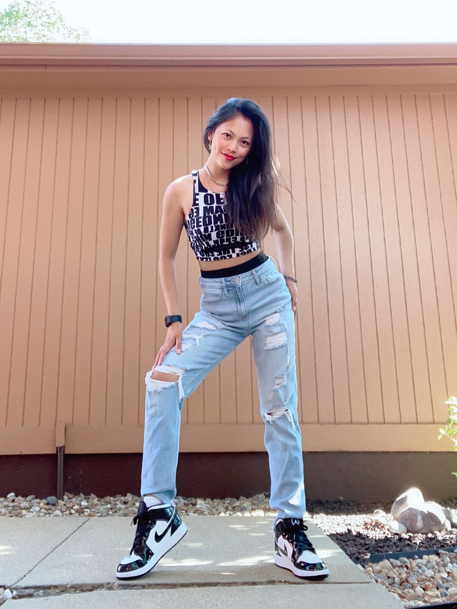 Casual street style outfit with ripped jeans and Nike sneakers against a beige wall.