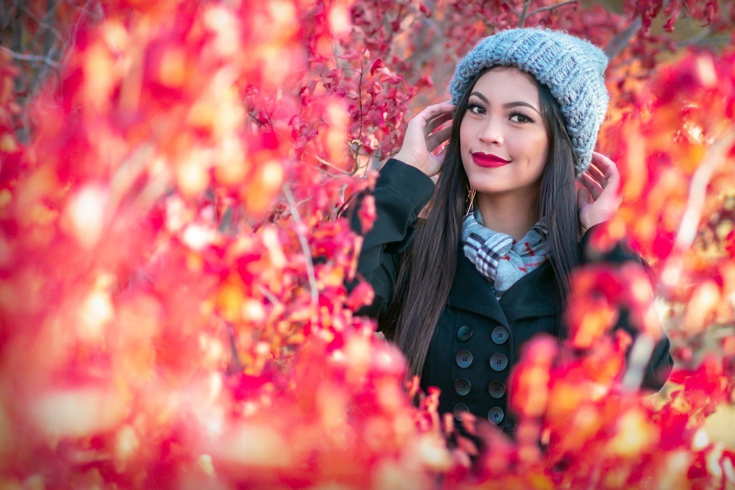 Autumn portrait through red foliage featuring a cozy gray knit beanie and dark coat.