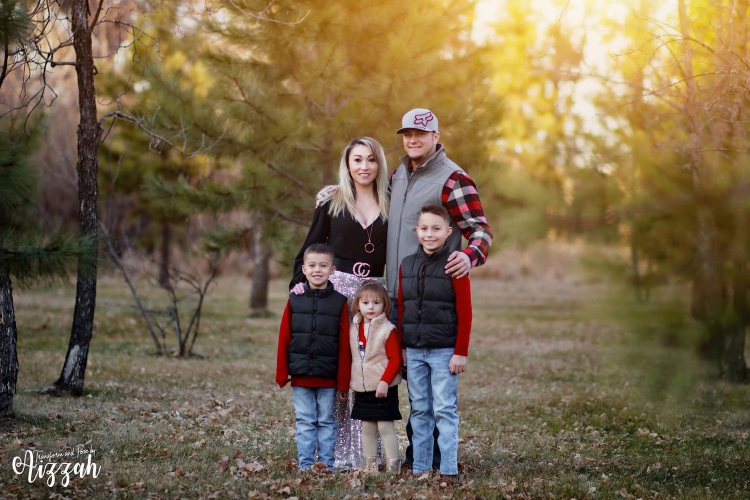 Family of five poses together at sunset in coordinated casual outfits against a wooded backdrop.