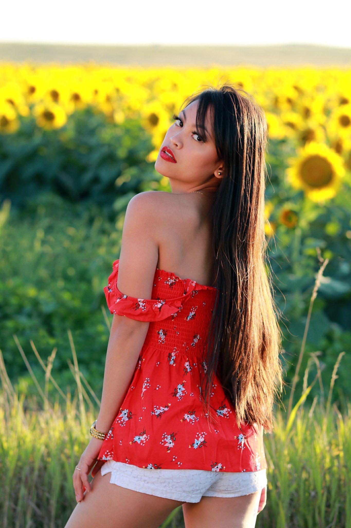 Summer portrait in a sunflower field wearing a red off-shoulder dress with flowers at sunset.