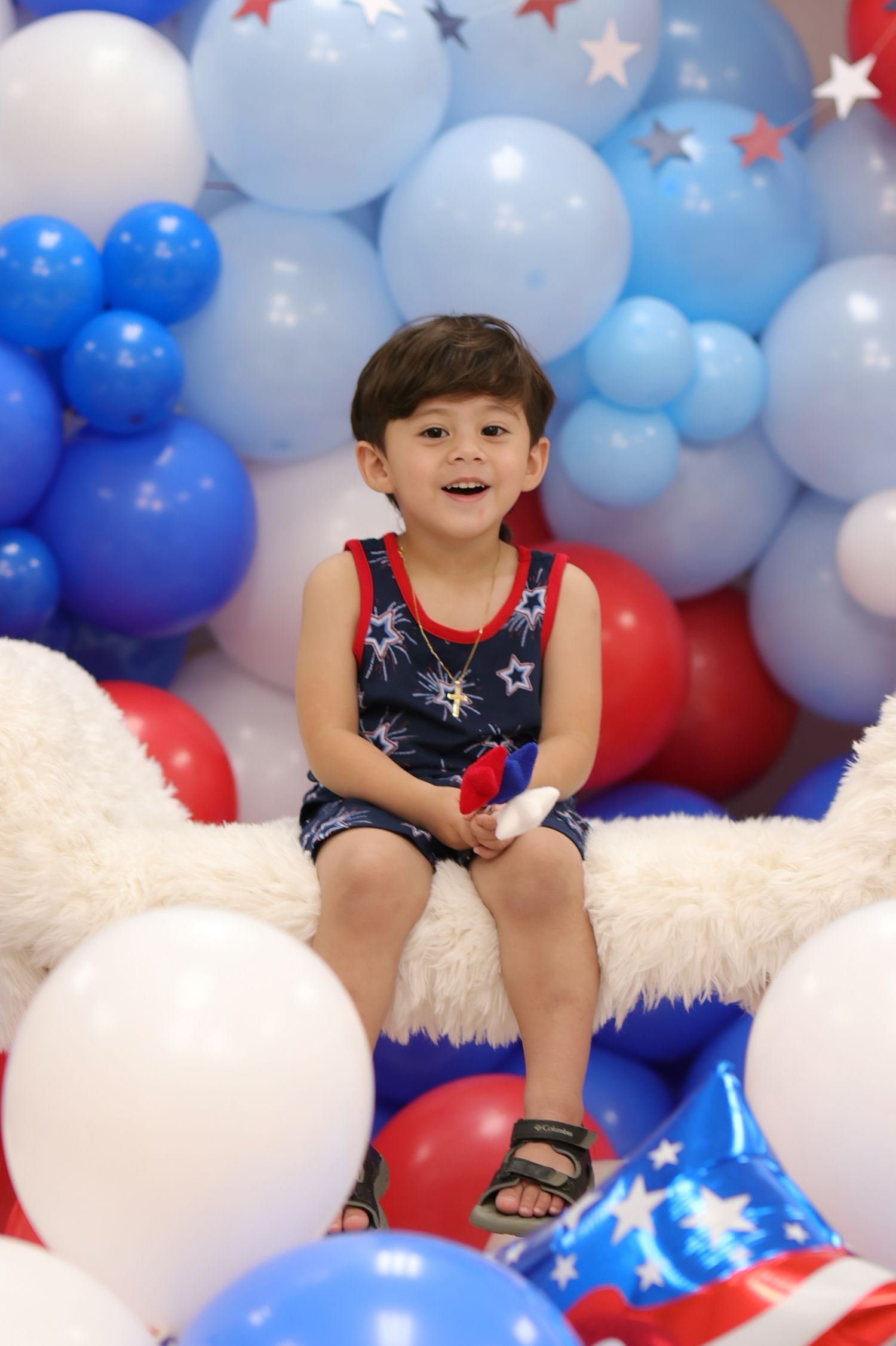 Child sitting among red, white and blue balloon decorations with patriotic theme.