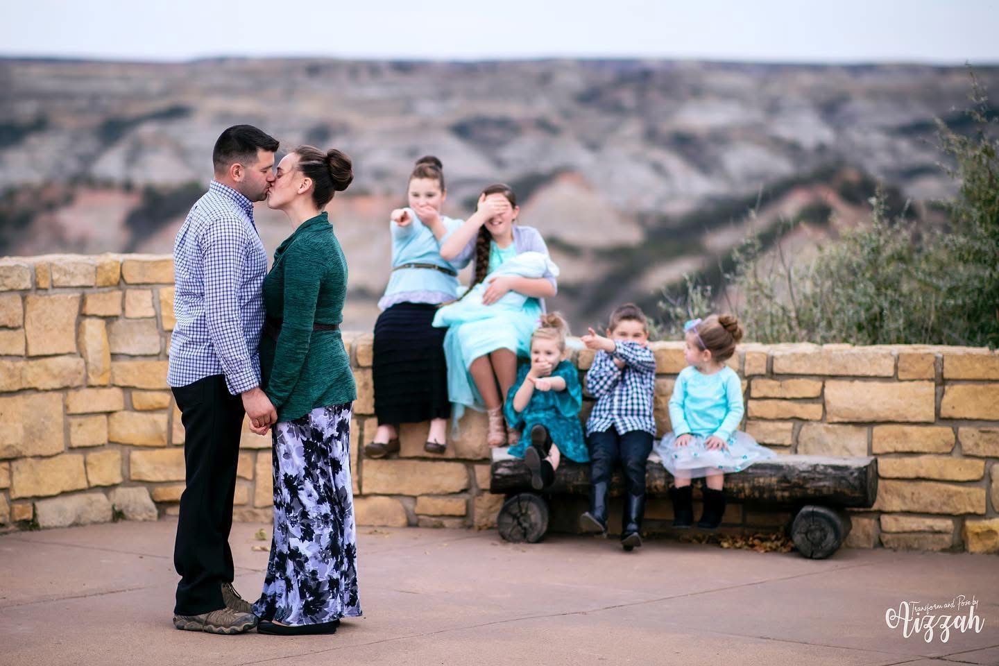 Family portrait at scenic overlook with children sitting on wooden wagon in background.