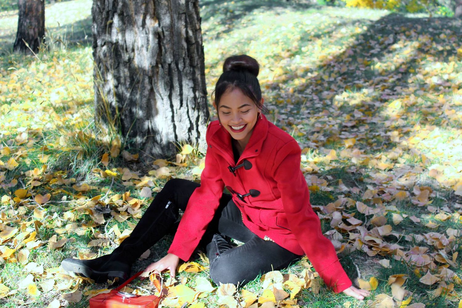 Autumn outdoor portrait with red jacket while sitting among fallen leaves.