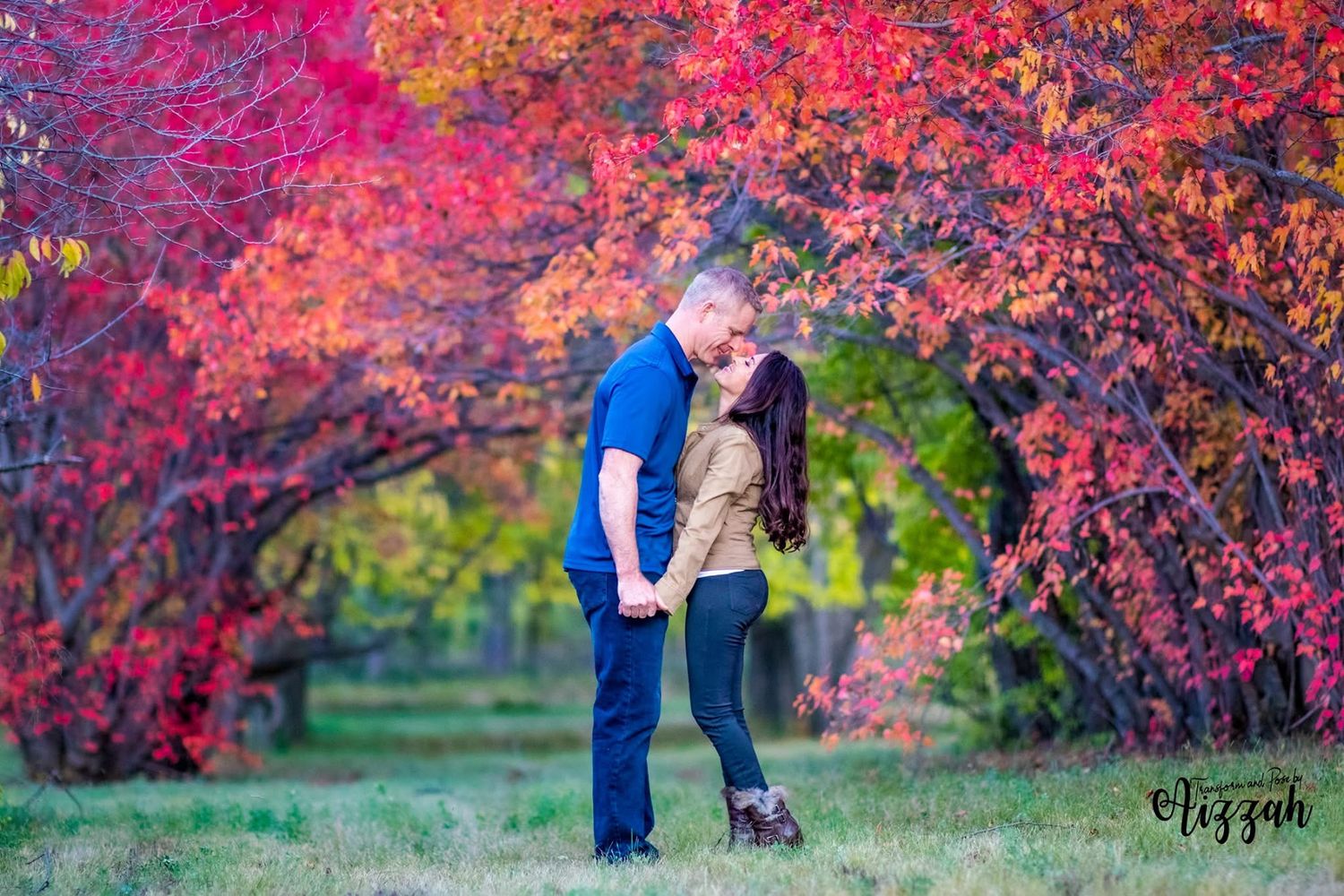 Romantic couple embracing under vibrant red fall foliage in a park setting.