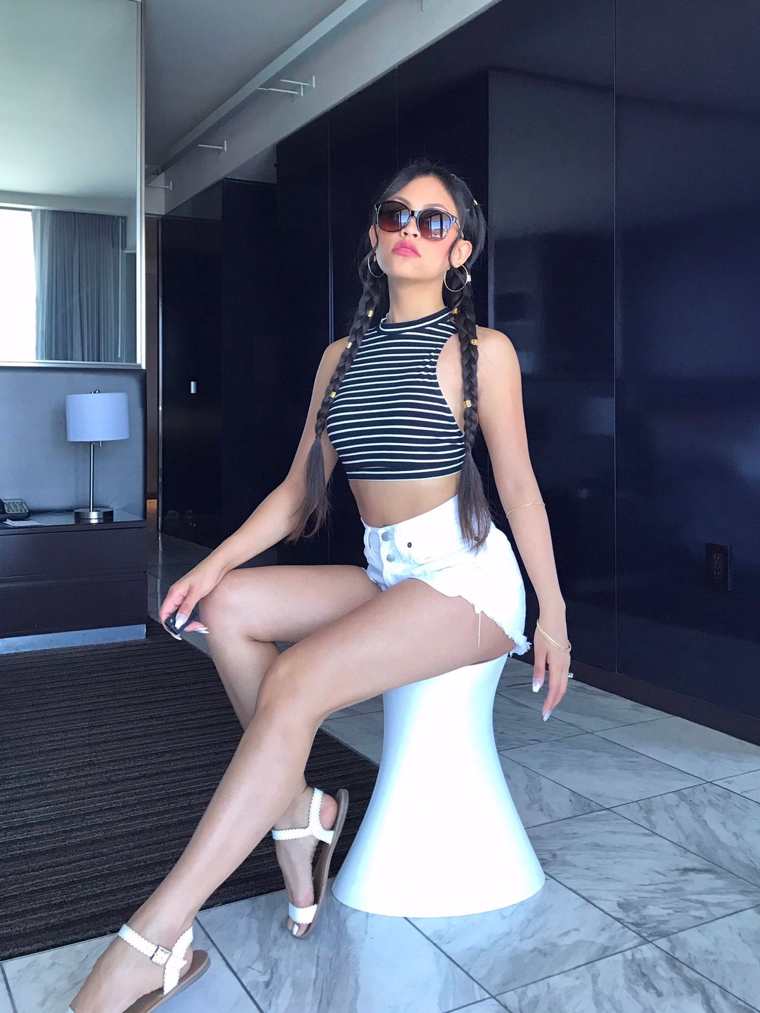 Modern indoor fashion photo with someone in casual wear posing on a white decorative stool.