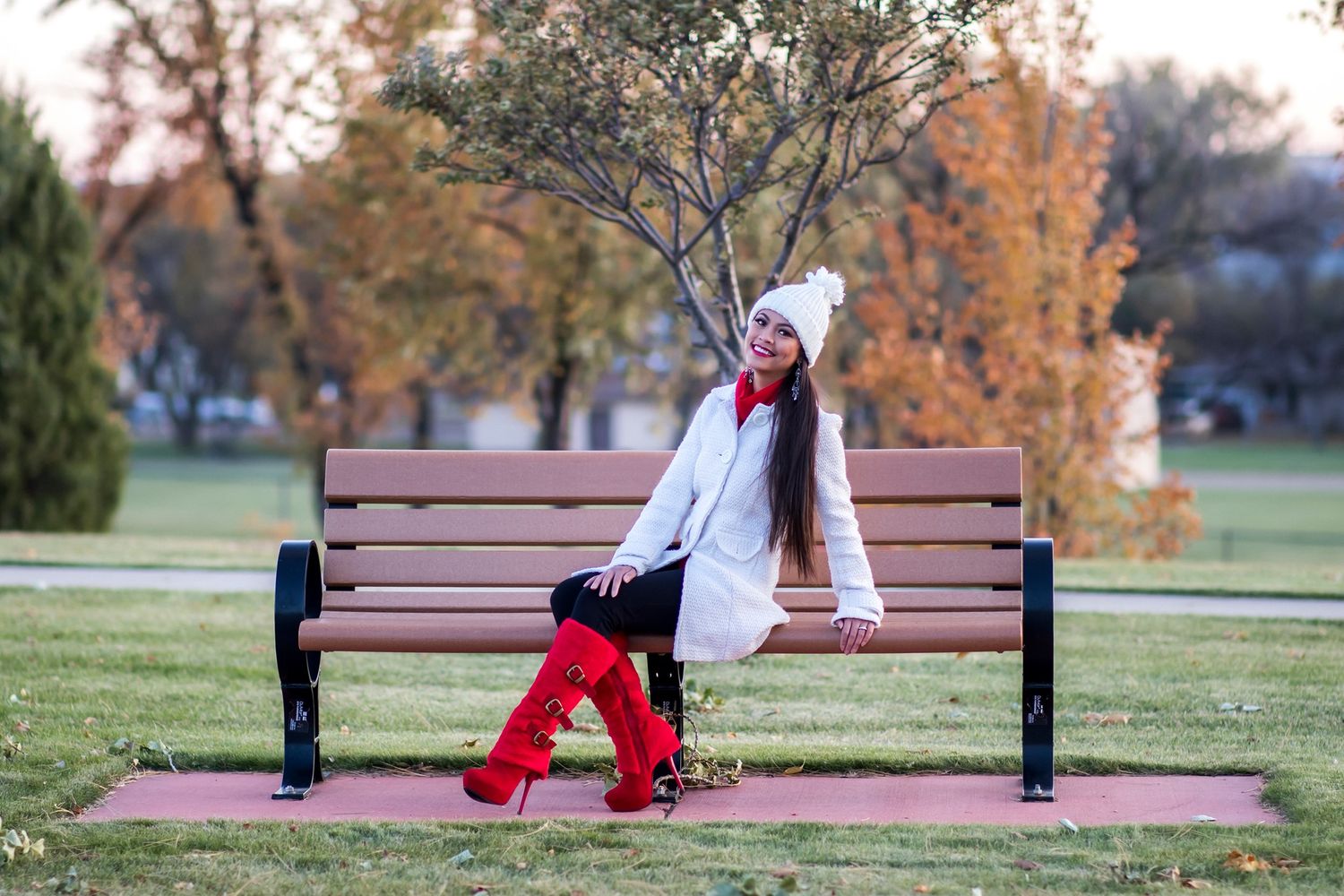 Winter fashion portrait on a park bench with red boots and white winter accessories.
