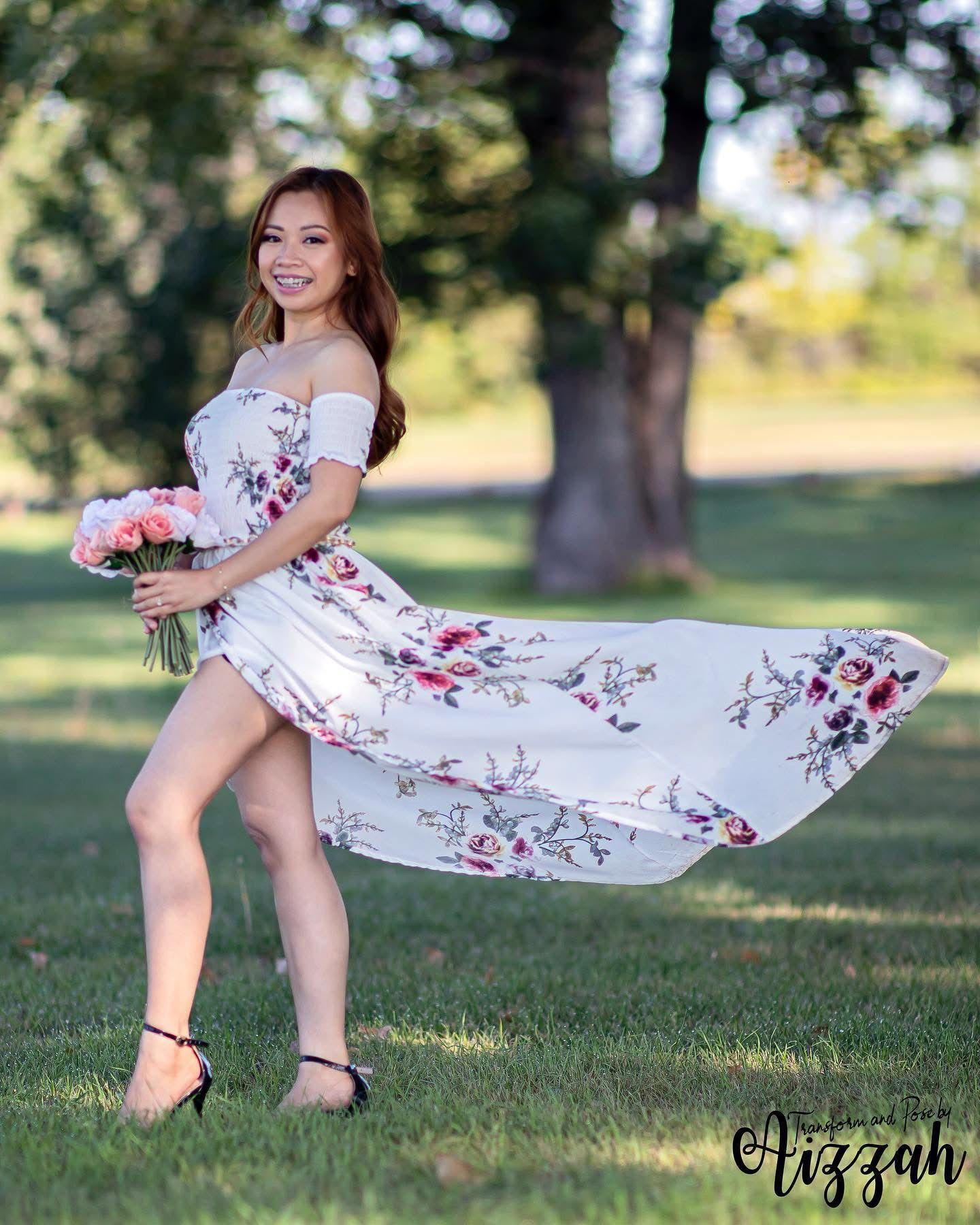 Woman in flowing floral dress twirling outdoors in a sunny park setting.